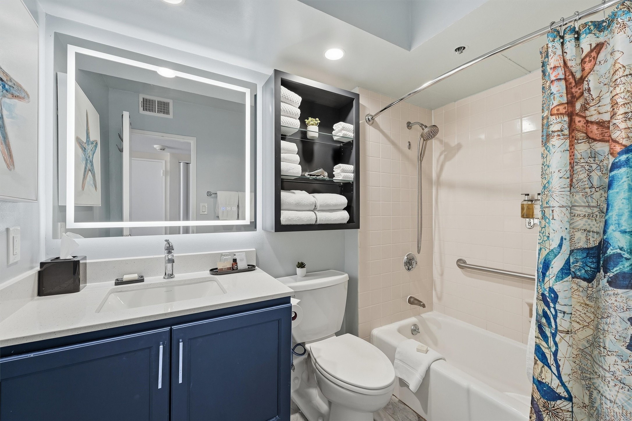 The bathroom features a navy vanity, illuminated mirror, and a convenient tub/shower combination.