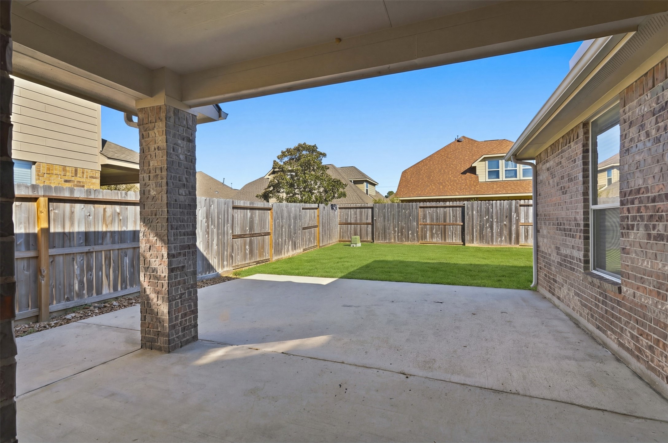 The covered patio overlooks a private, fenced backyard with lush green lawn, perfect for outdoor relaxation and entertainment.