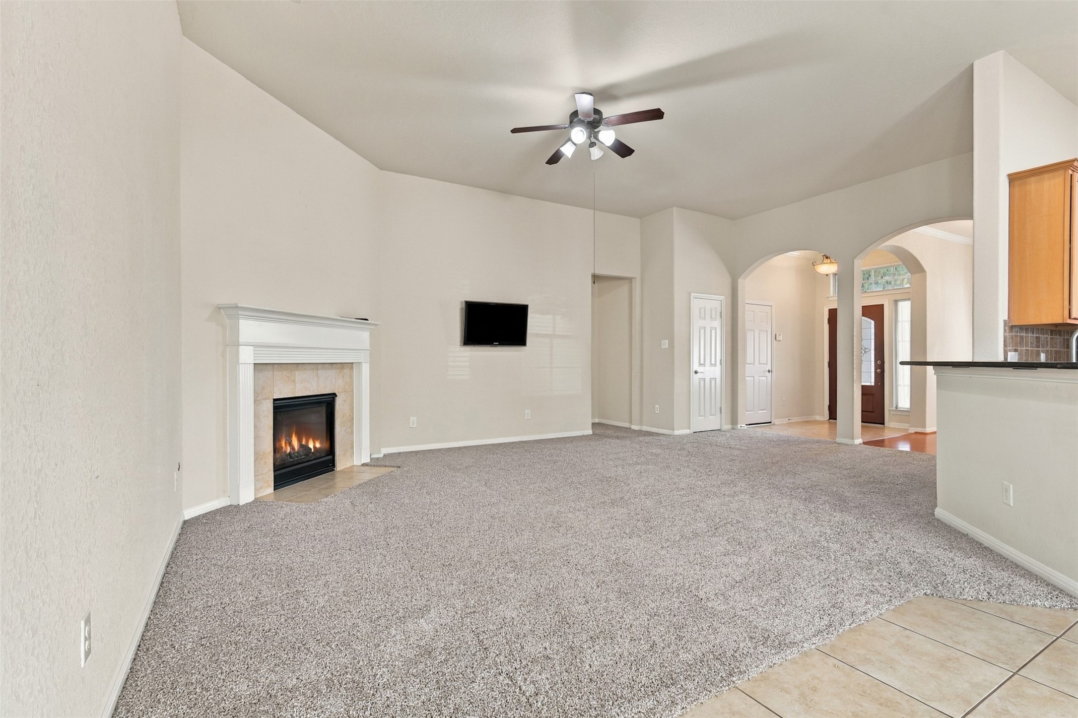 Another view of the living room featuring a cozy fireplace, plush carpeting, and elegant arched doorways leading to additional living areas.