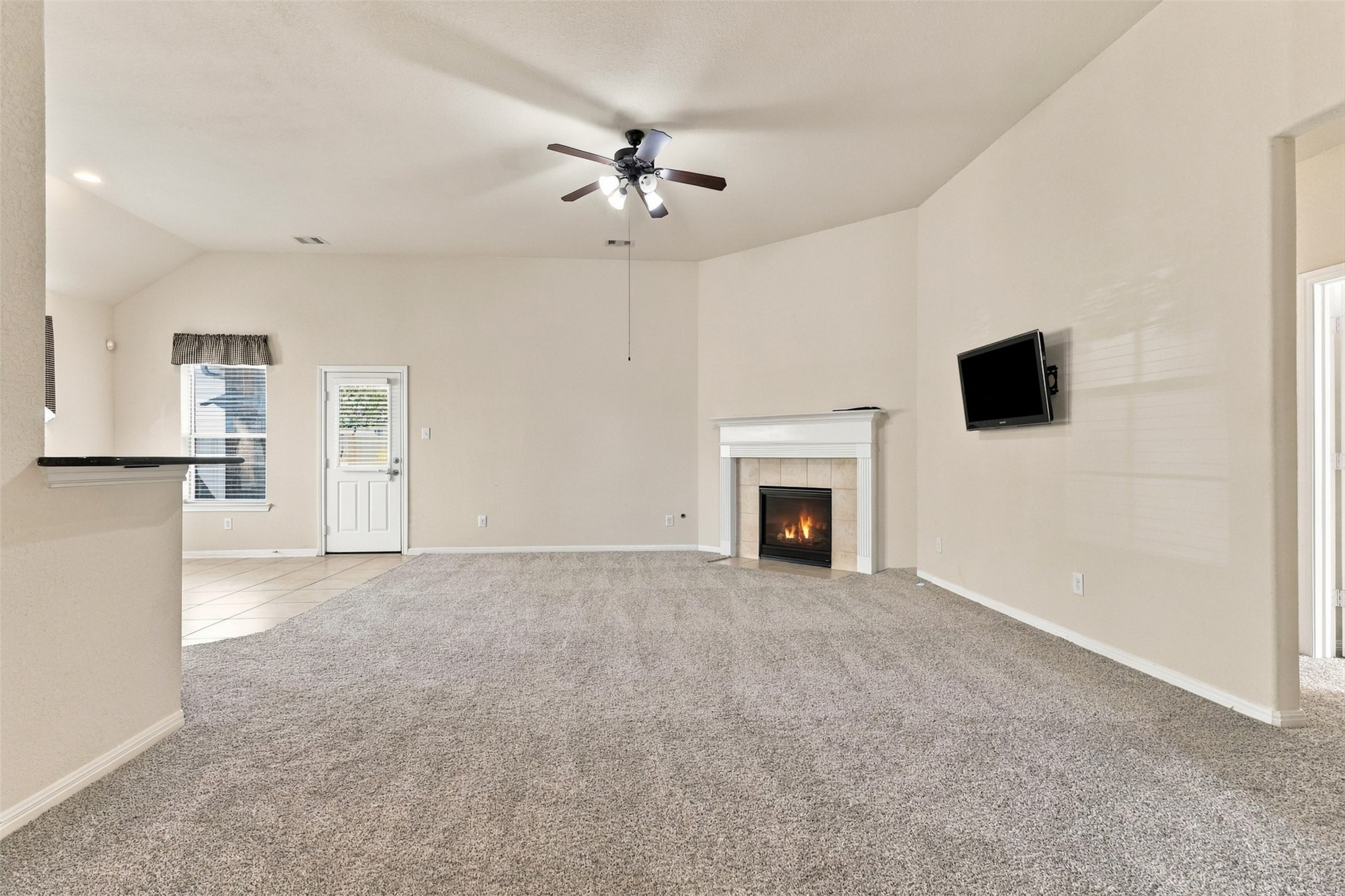 Spacious living room with a cozy fireplace, plush new carpeting (2026), and a ceiling fan, offering a warm and inviting atmosphere.