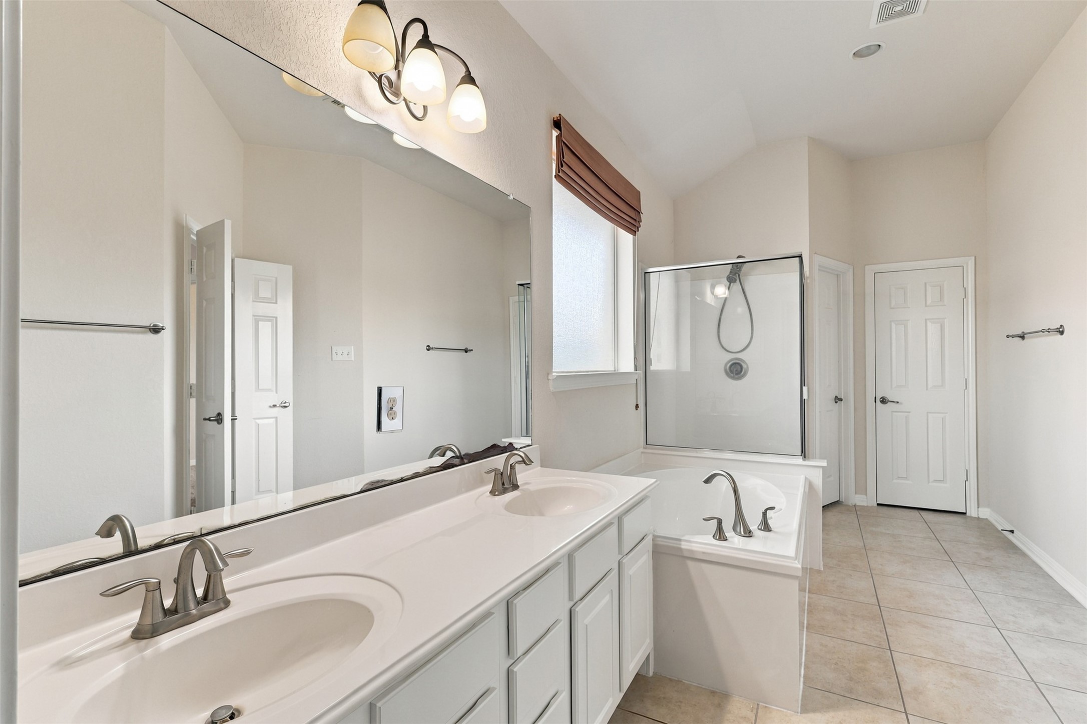Bright bathroom featuring a double vanity, large mirror, and elegant fixtures, complemented by a separate glass-enclosed shower and soaking tub.