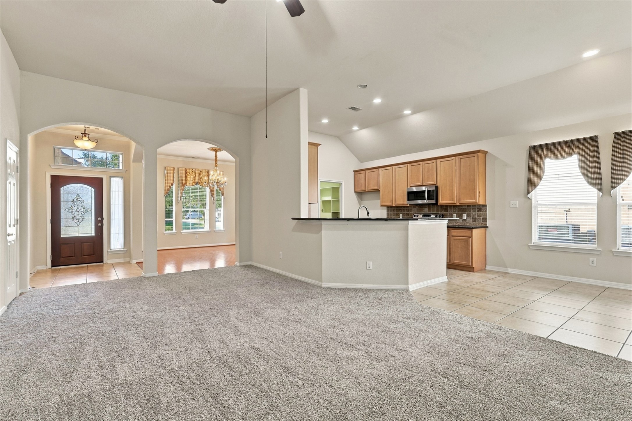 Spacious open-concept living area with plush carpeting, high ceilings, and abundant natural light, seamlessly connecting to a modern kitchen with ample cabinetry and a cozy breakfast bar.