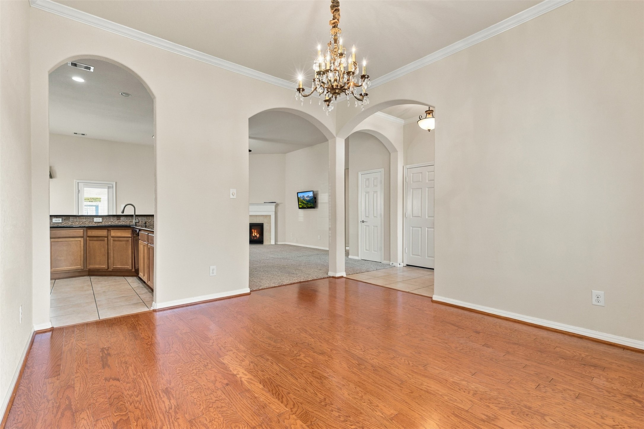 Another view of the dining rooms with hardwood floors, an ornate chandelier, and arched doorways leading to a cozy kitchen and living area with a fireplace.