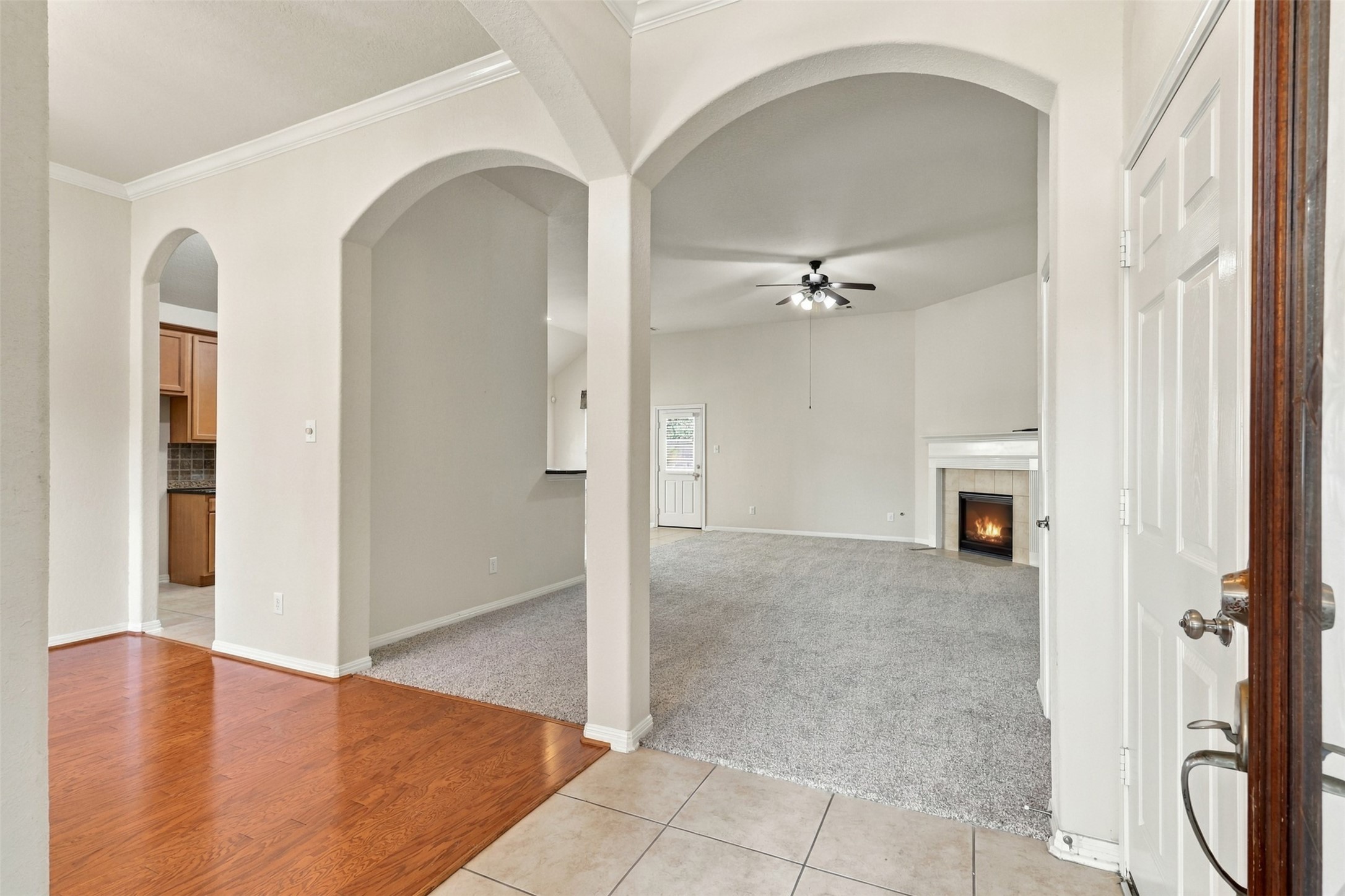 Inviting open-concept living area featuring arched doorways, a cozy fireplace, and a mix of tile and hardwood flooring, creating a warm and welcoming atmosphere.