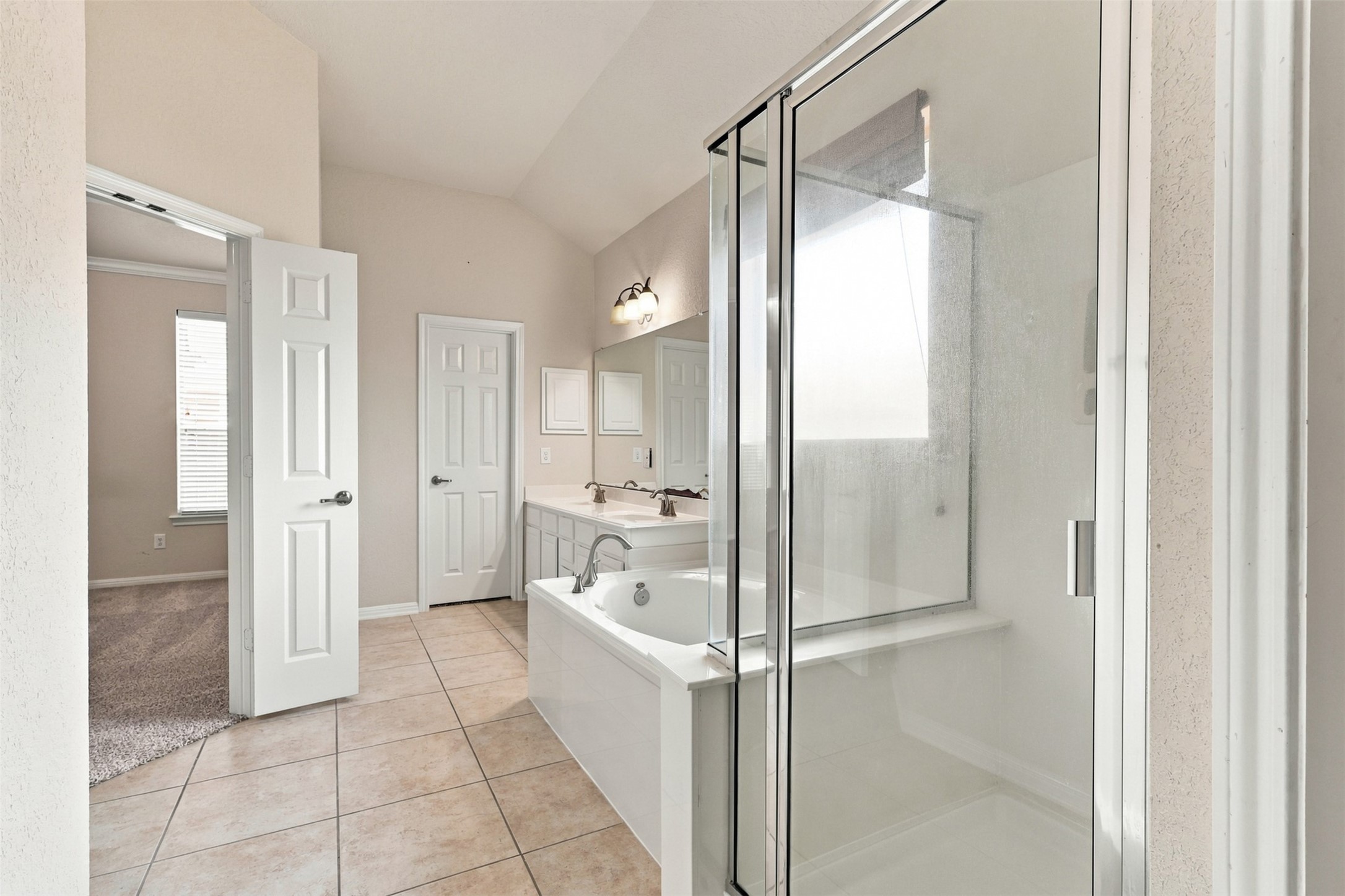 Elegant bathroom featuring a spacious glass-enclosed shower and a relaxing bathtub, complemented by dual sinks and ample natural light.