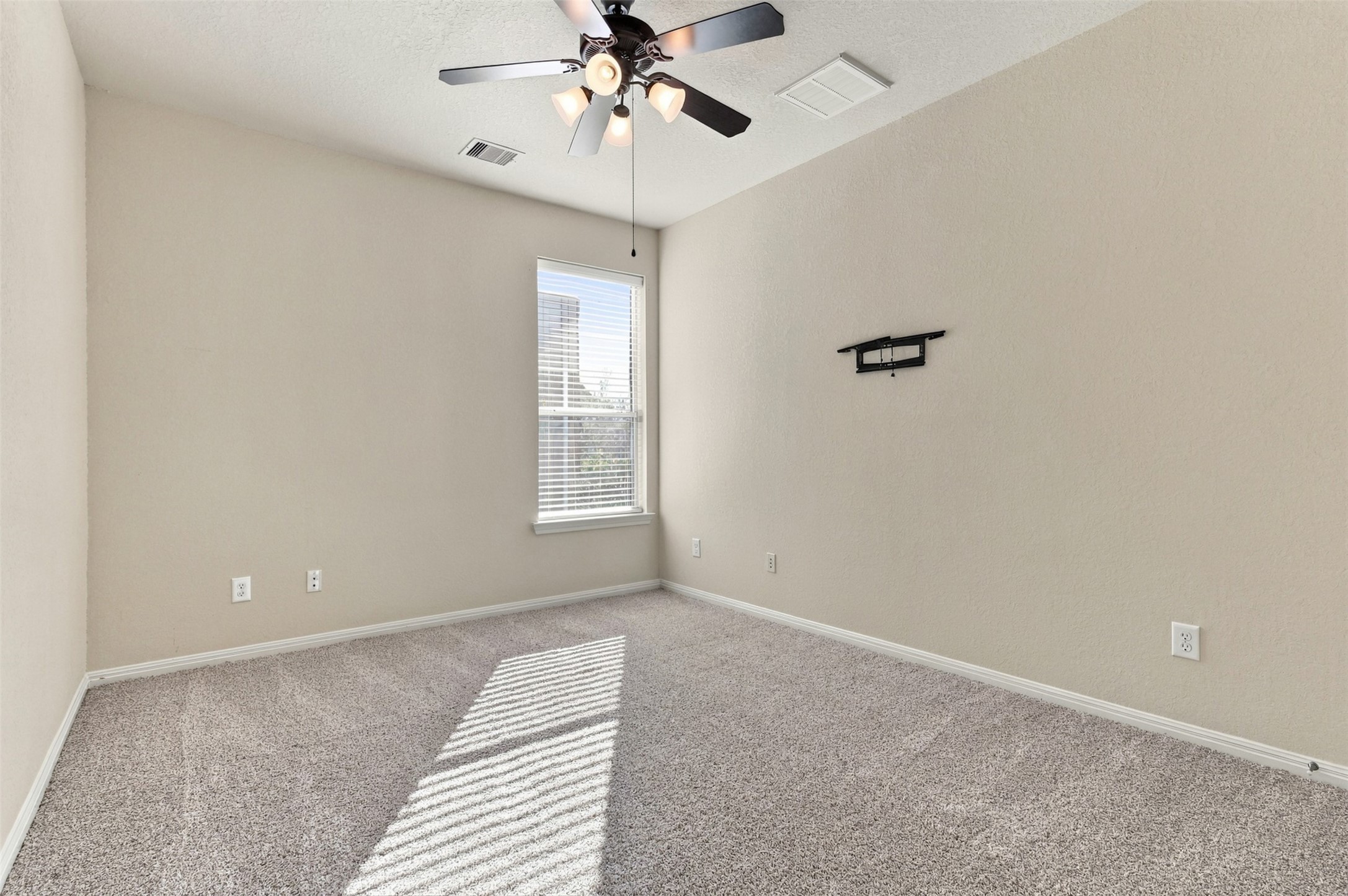 Bright and inviting bedroom featuring plush carpeting, a modern ceiling fan, and ample natural light streaming through a large window.