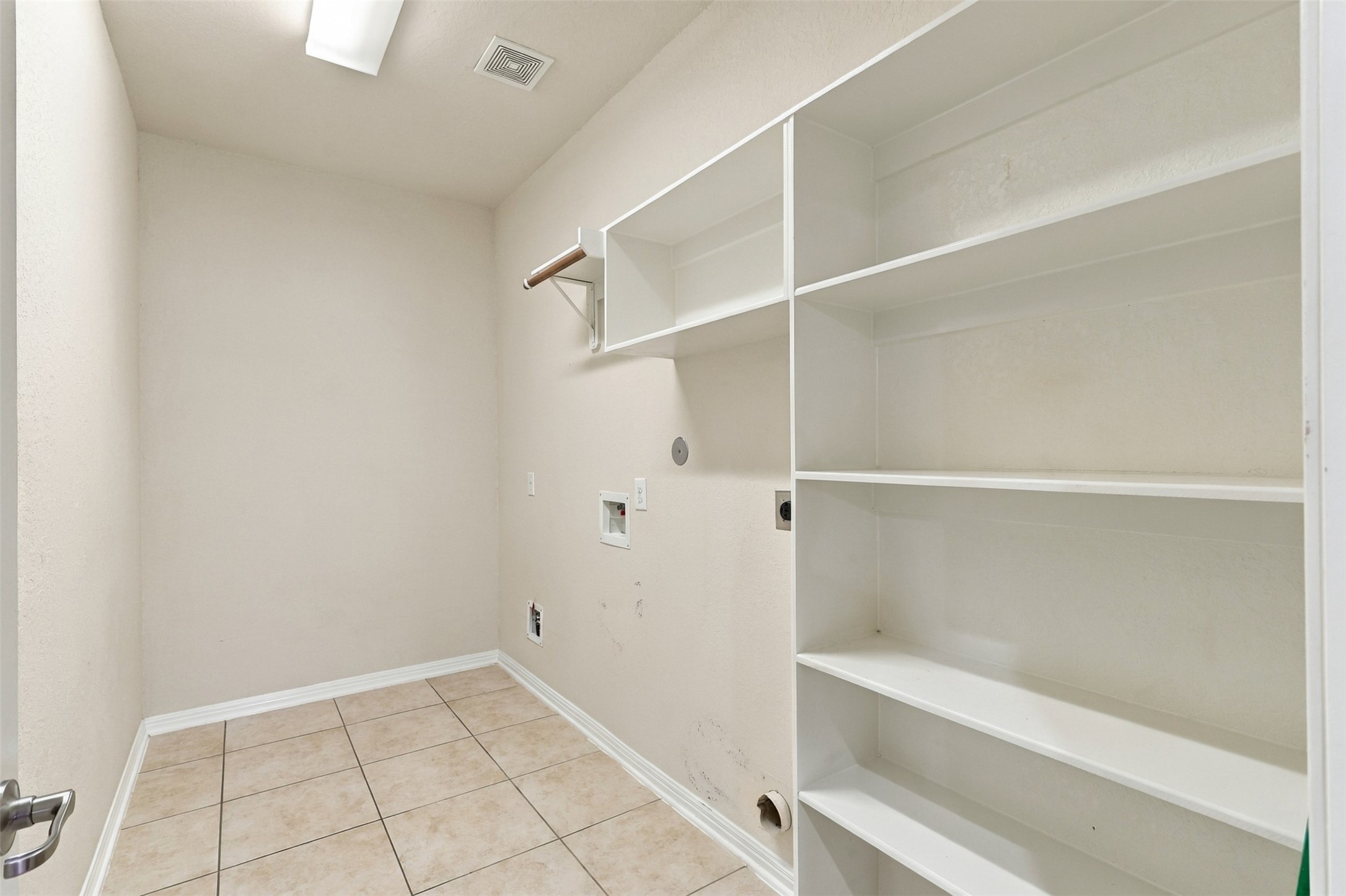 Spacious laundry room with built-in shelving and tile flooring, offering ample storage and functionality.