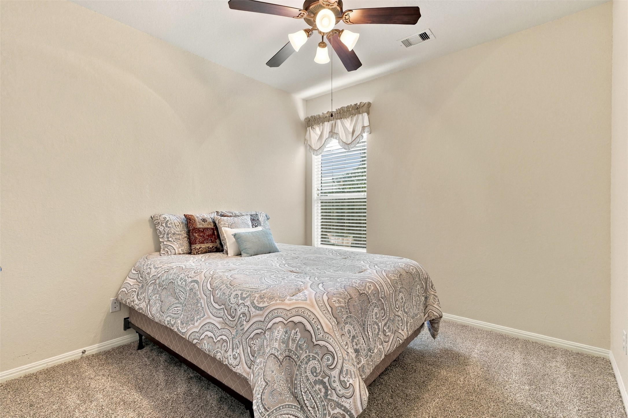 Cozy bedroom featuring neutral tones, plush carpeting, and a ceiling fan, offering comfort and style.