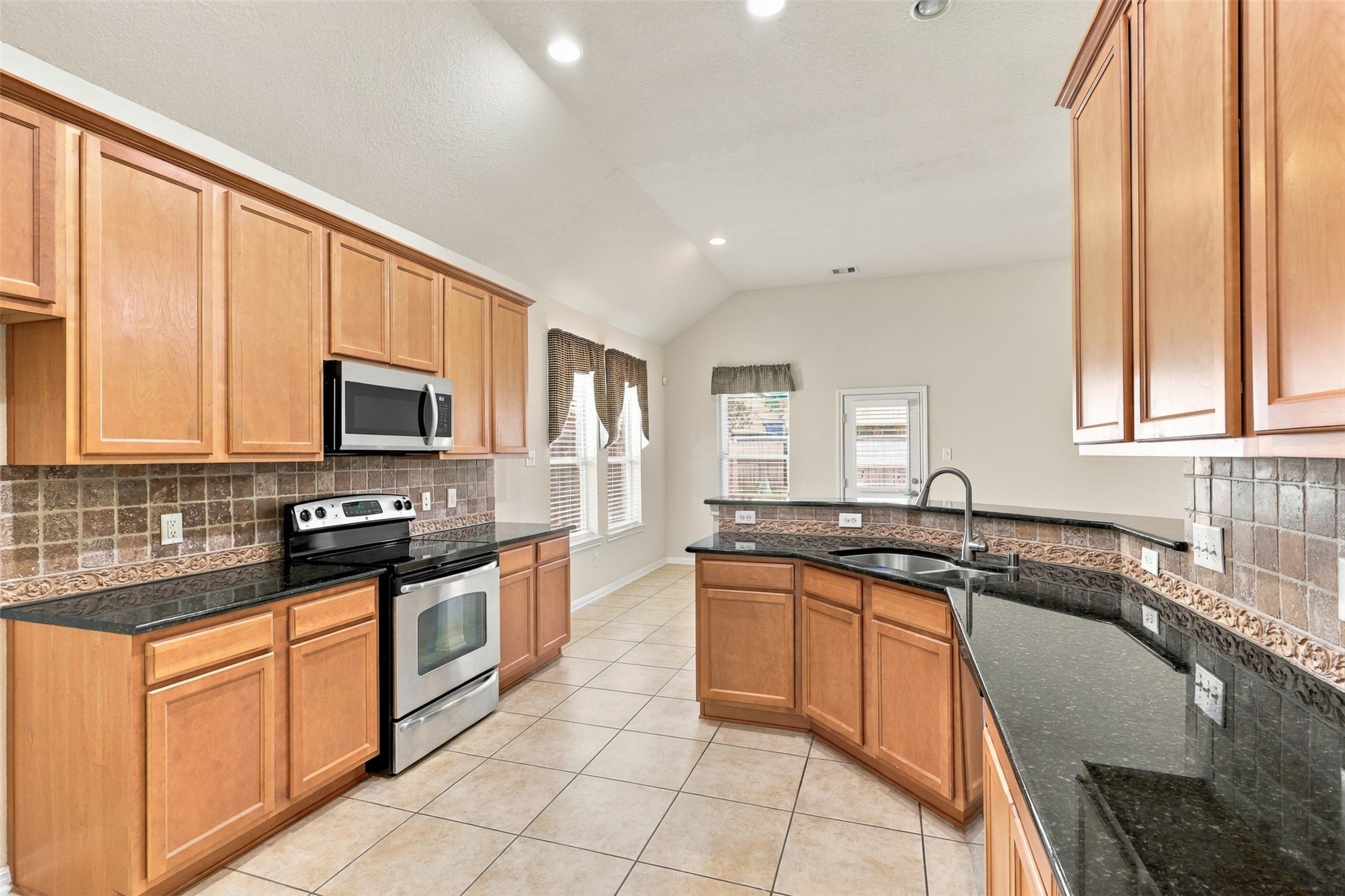 This kitchen features sleek granite countertops, stainless steel appliances, and warm wood cabinetry, complemented by a stylish tile backsplash and ample natural light.