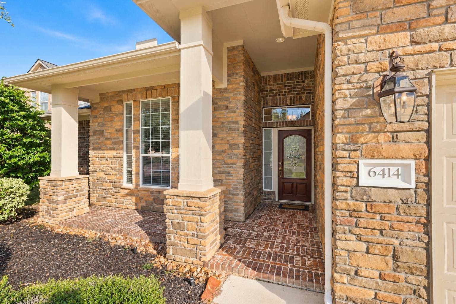 Stone and brick facade with an inviting covered entryway and elegant glass front door, enhanced by classic lantern-style lighting.