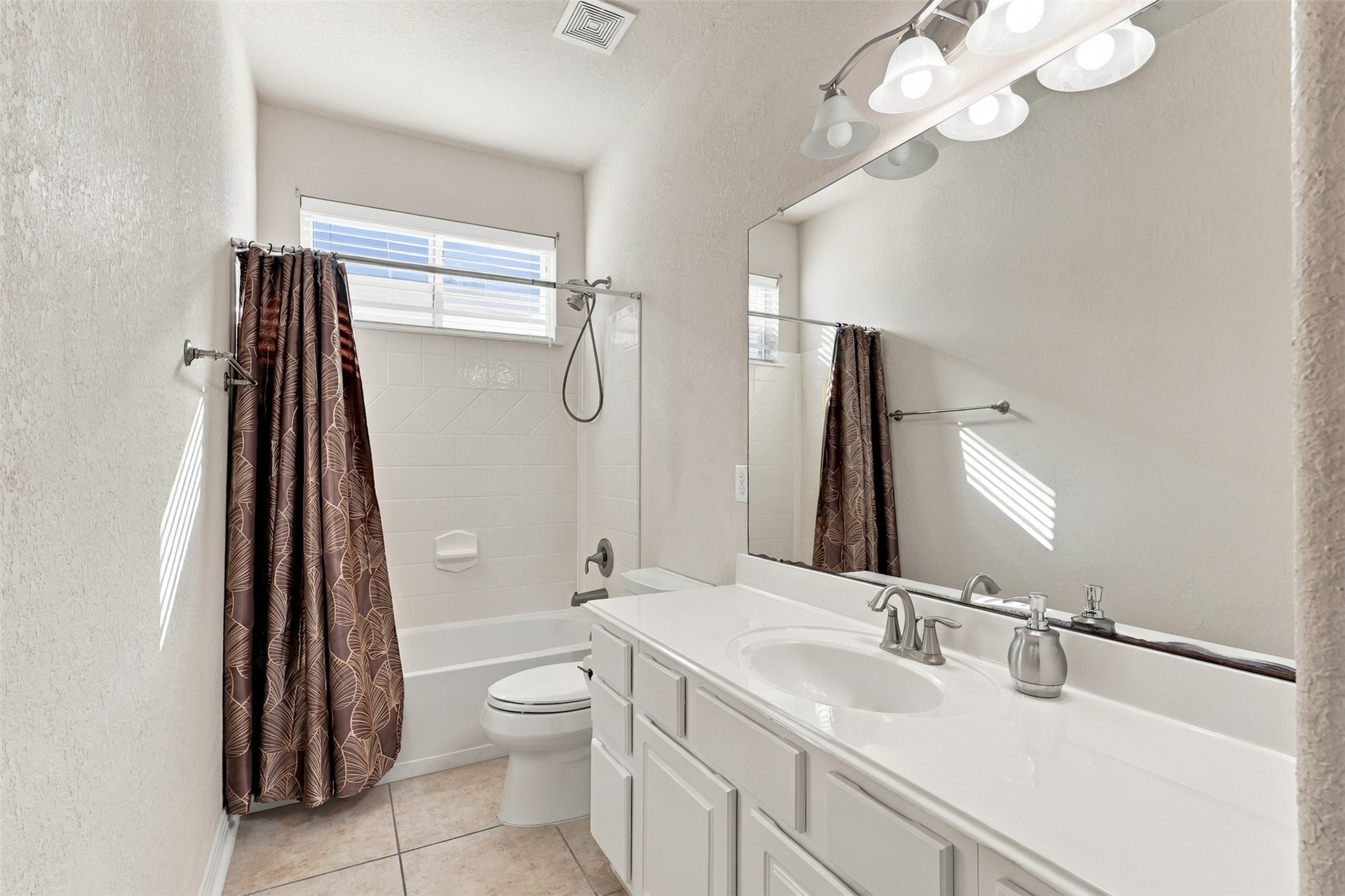 Bright and inviting bathroom featuring a spacious vanity, elegant fixtures, and a shower-tub combo with a stylish curtain.