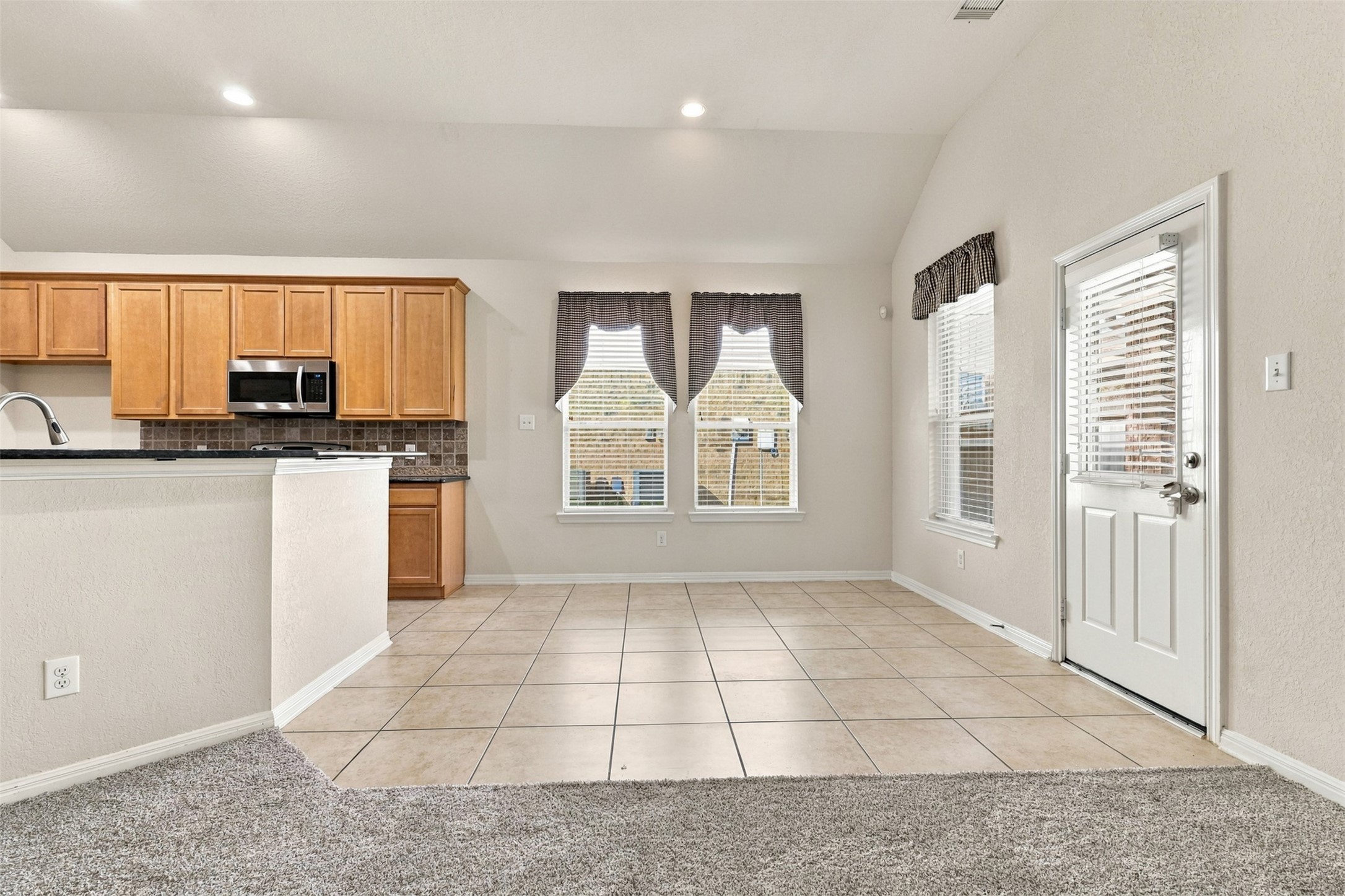 Bright open concept kitchen and dining area with natural light, featuring wood cabinetry, modern appliances, and a convenient tile floor layout.