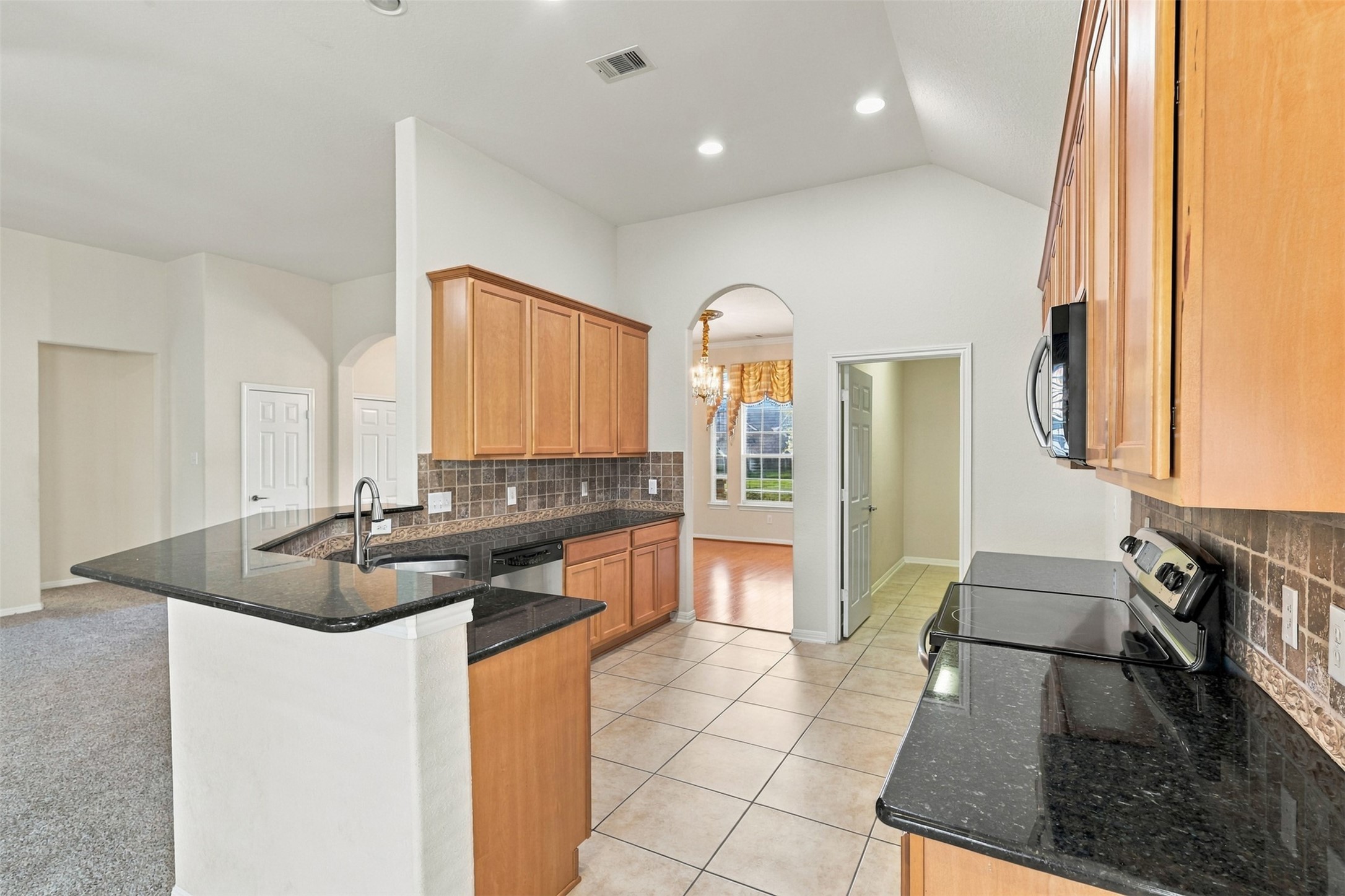 Modern kitchen with sleek granite countertops, ample cabinetry, and stainless steel appliances, seamlessly flowing into a spacious, light-filled dining area.