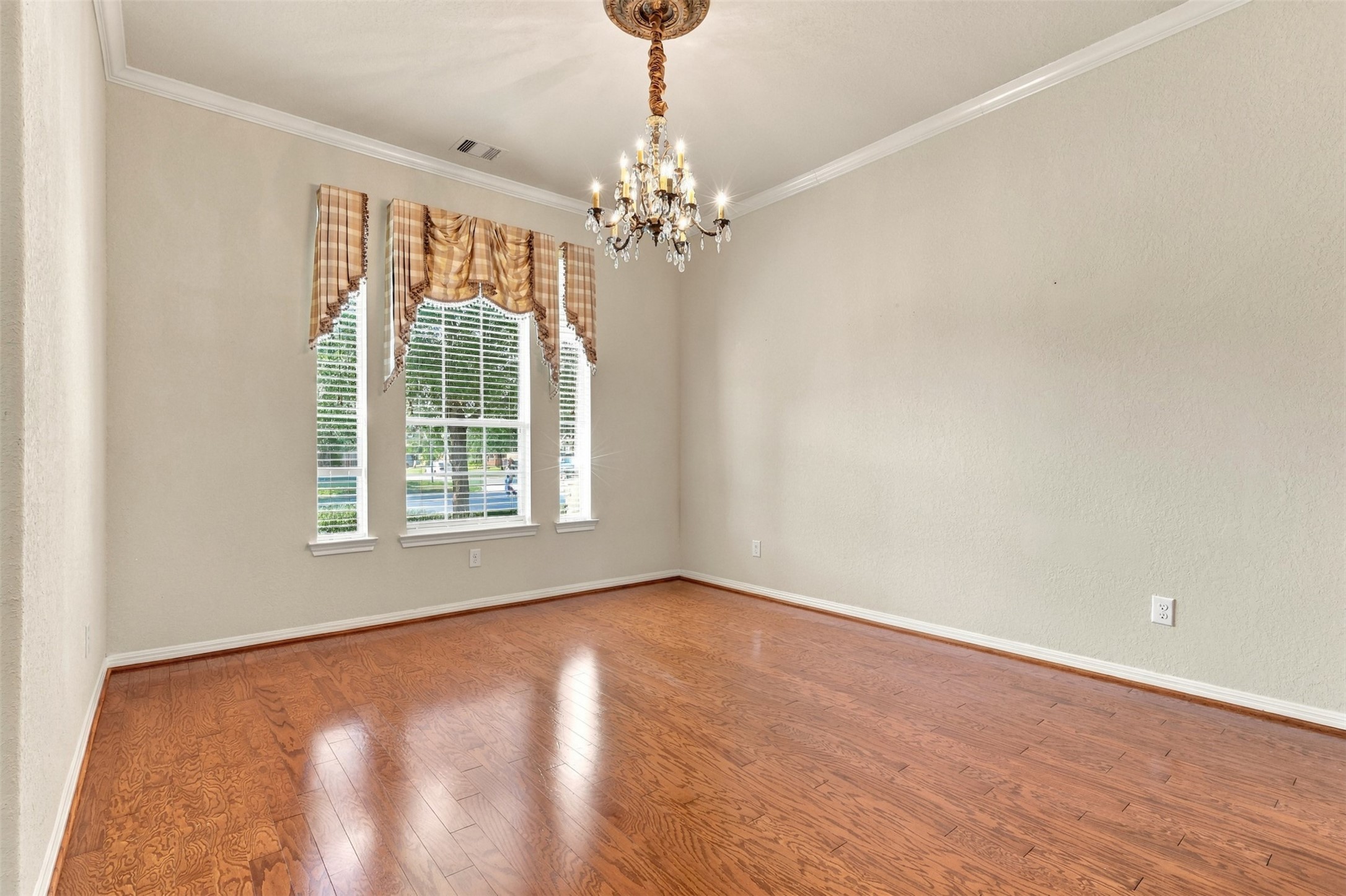 Elegant dining room featuring rich hardwood floors, a charming chandelier, and large windows with classic drapery, offering ample natural light.