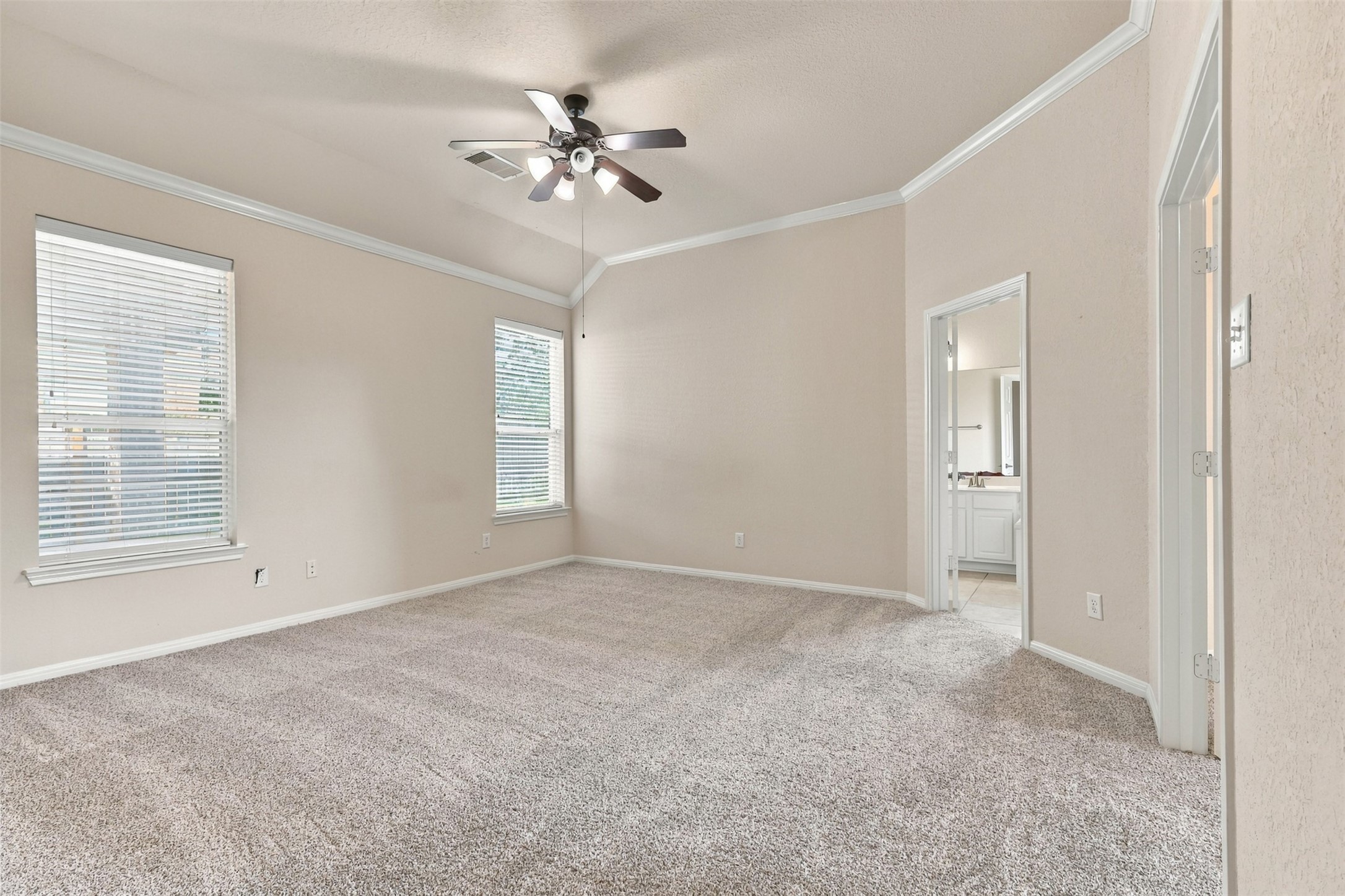 Spacious primary bedroom with plush carpet, high ceilings, and abundant natural light from large windows, featuring an elegant ceiling fan and direct access to a bright en-suite bathroom.