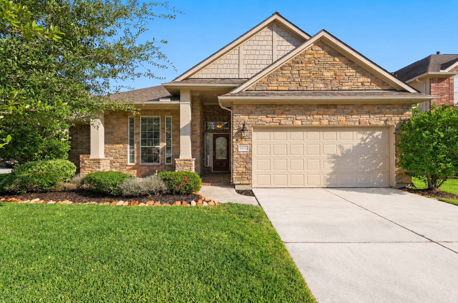 Charming stone-accented home with a welcoming front porch, manicured landscaping, and a spacious two-car garage.