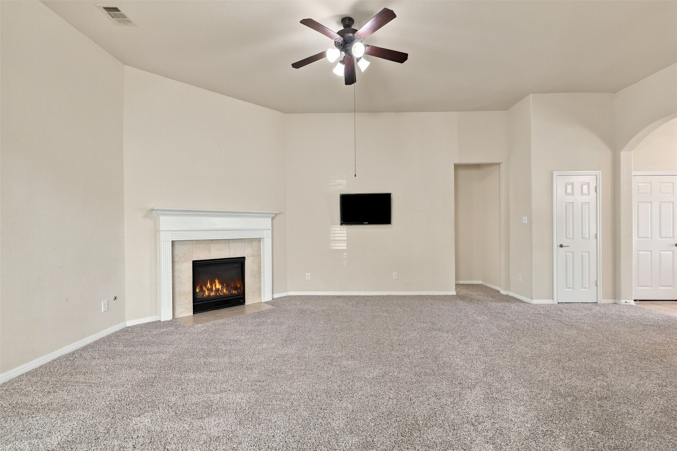 Spacious living room with plush carpet, featuring a cozy fireplace and ceiling fan, perfect for relaxation and entertainment.
