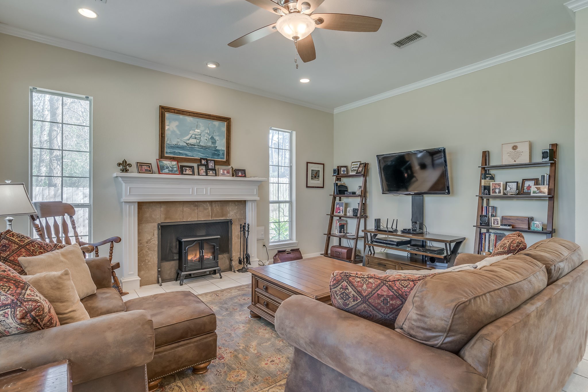 Discover the perfect blend of elegance and comfort in this charming family room, featuring tiled flooring, ceiling fan, crown molding, and cozy wood-burning fireplace with gas connections