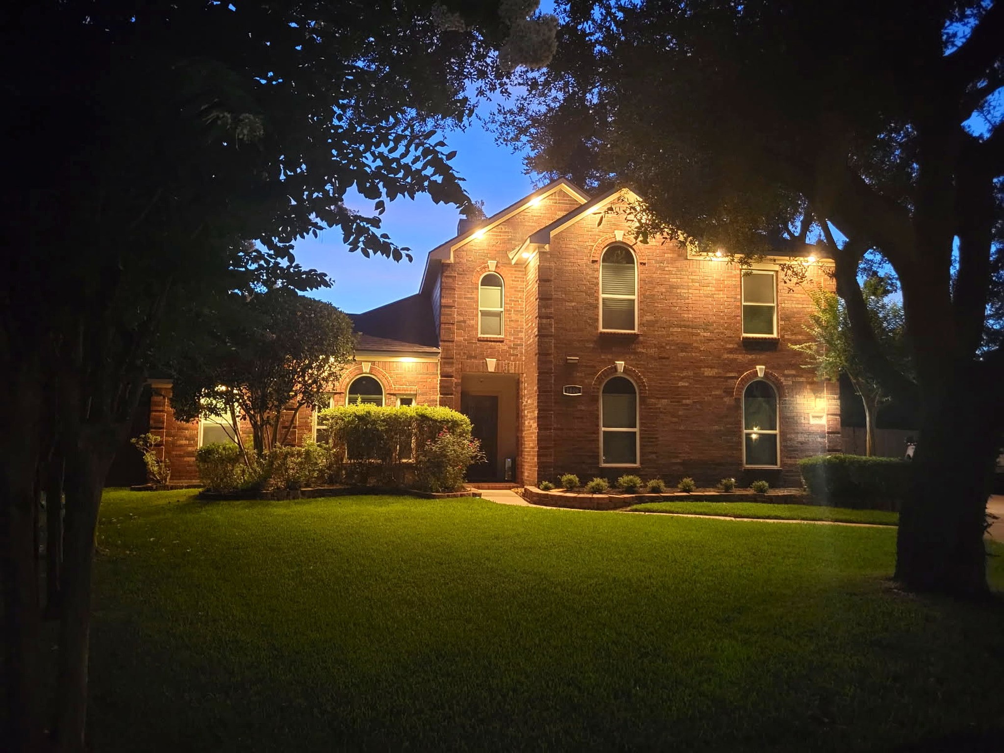 Elegant exterior lighting accents the brick facade and rooflines at dusk.