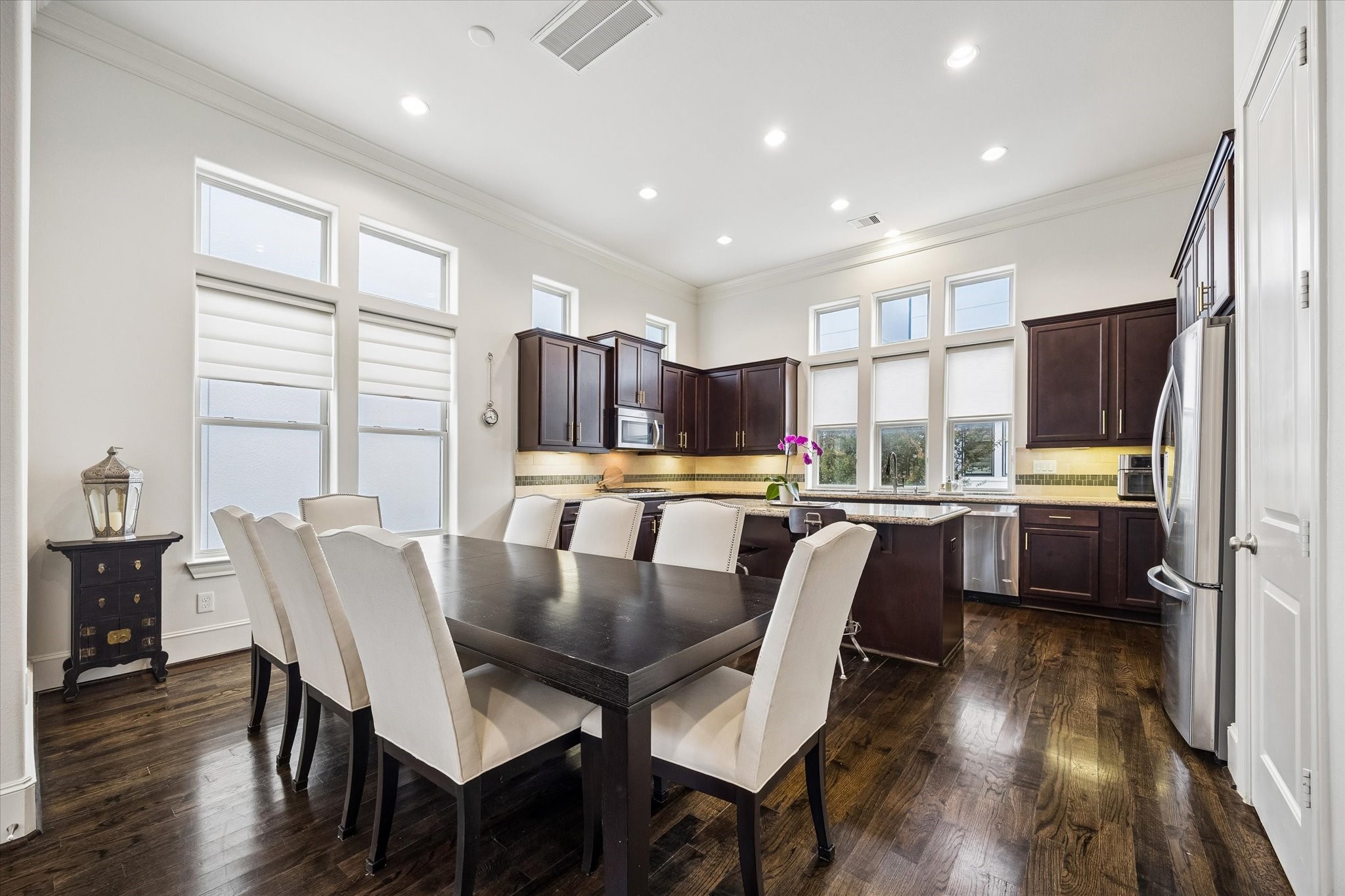 Abundant windows and recessed lighting keep the kitchen and dining area bright, while rich cabinetry and hardwood floors add warmth throughout. An oversized island creates a natural gathering point with plenty of room for meal prep and casual seating.