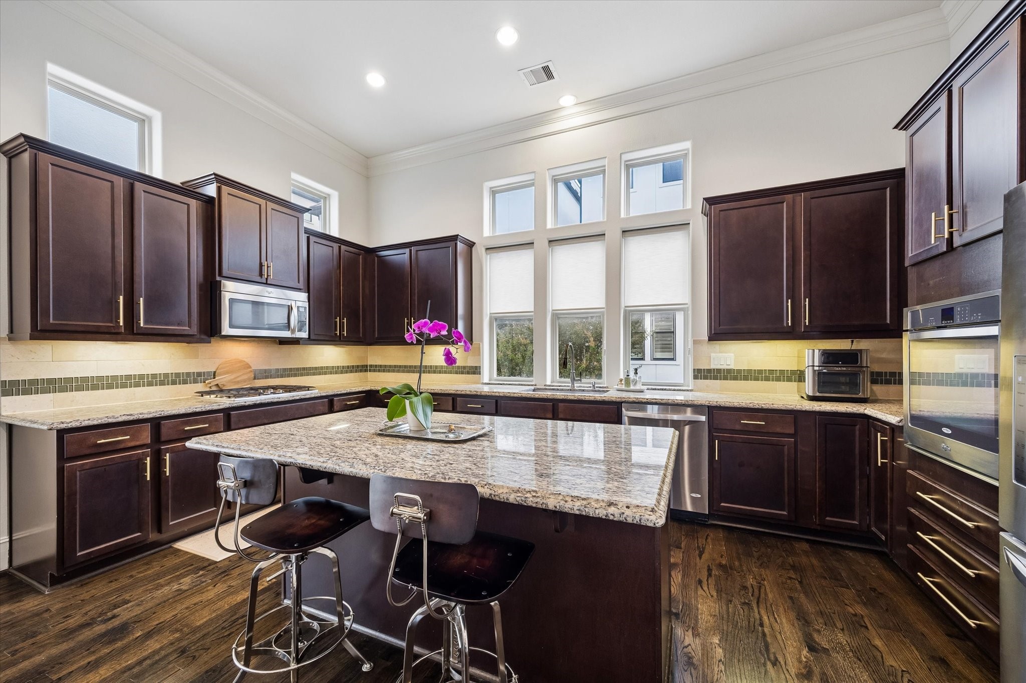 Granite countertops wrap the spacious kitchen, pairing with rich wood cabinetry, stainless steel appliances, and under cabinet lighting. A large center island adds additional prep space and seating, while windows above the sink bring in natural light.