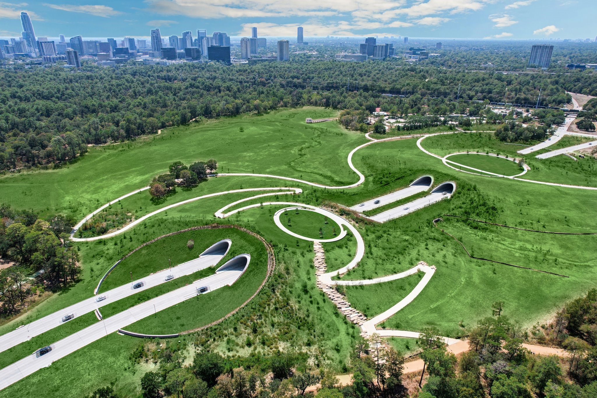 Aerial view of Memorial Parks Land Bridge, connecting miles of hike and bike trails across 100 acres of preserved green space, with downtown Houston skyline in the distance.
