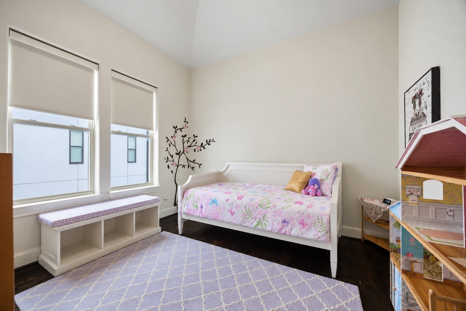 Vaulted ceilings and paired windows bring natural light into this secondary bedroom, while dark hardwood floors add warmth and contrast.