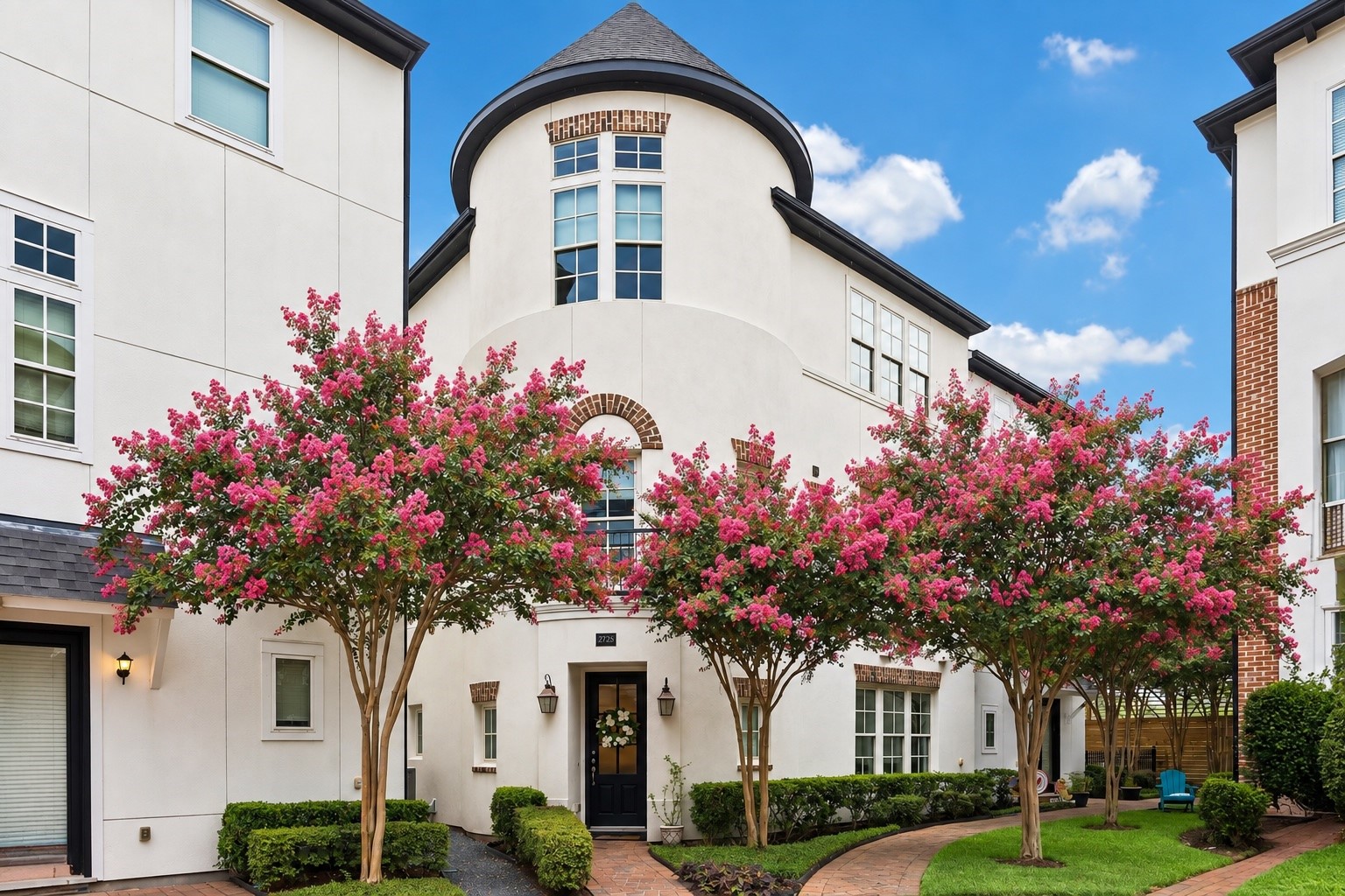 Classic architecture meets a lush courtyard setting, where vibrant crepe myrtles frame the distinctive stucco faade and turret inspired roofline.