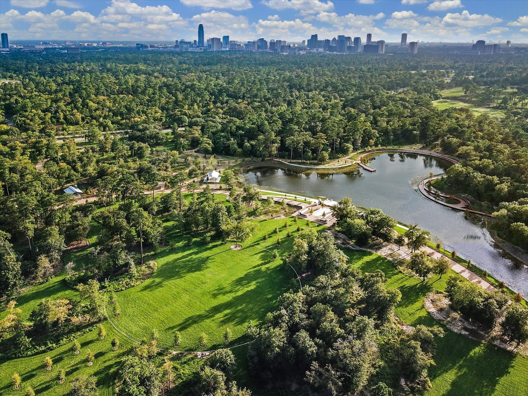 Aerial view of Memorial Park showcasing the iconic Land Bridge, expansive green space, and miles of hike and bike trails, with the Houston skyline visible in the distance.