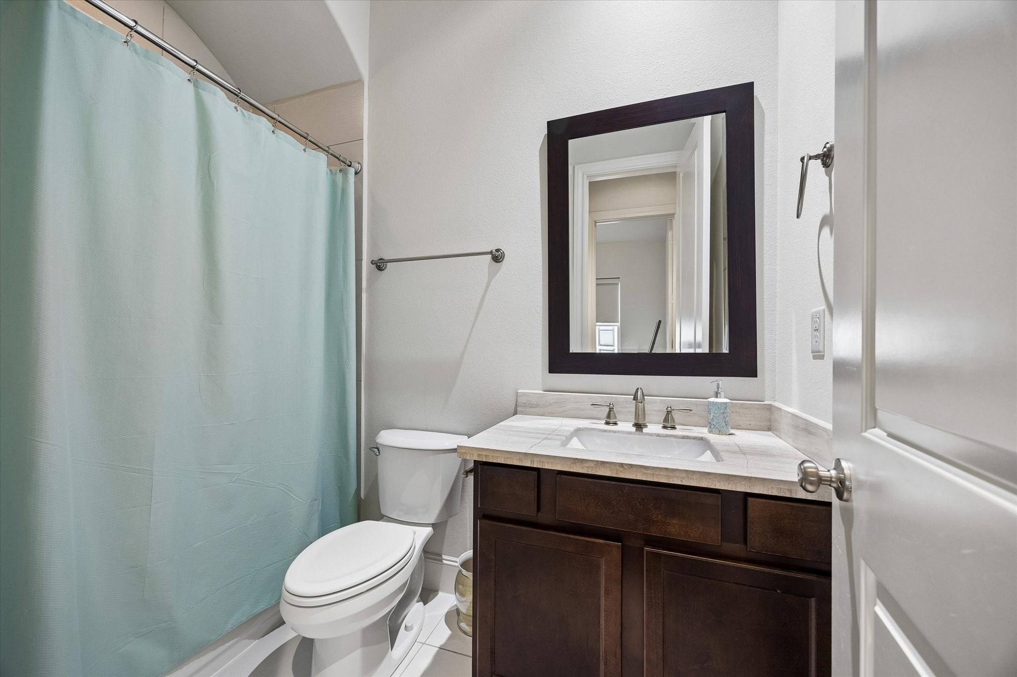 Well appointed secondary bath features a stone topped vanity, dark wood cabinetry, and a tub and shower combination, offering a private and comfortable setup for guests or family.