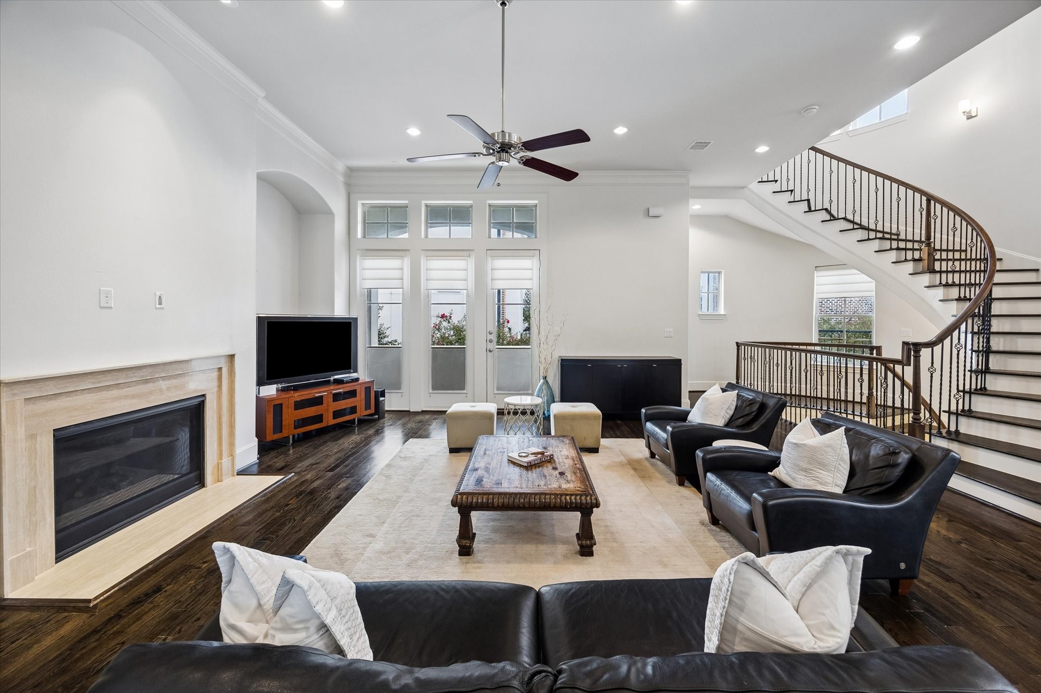 Natural light fills the living room, where rich hardwood floors and a stone fireplace bring warmth to the open layout. French doors and the sweeping staircase add architectural interest while connecting the homes main living spaces.