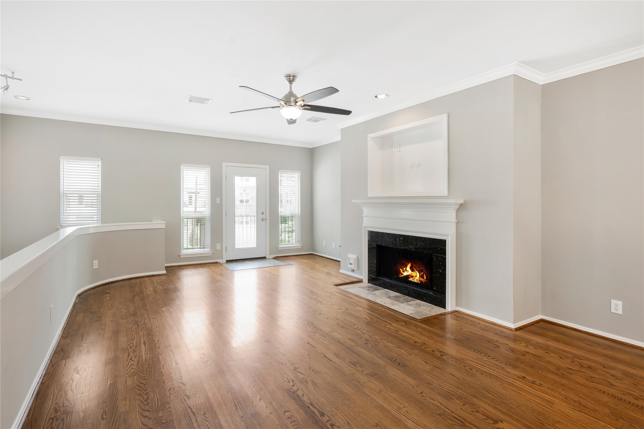 Living area with wood flooring, fireplace , ceiling fan and balcony with front view. Living area with wood flooring, fireplace , ceiling fan and balcony with front view.