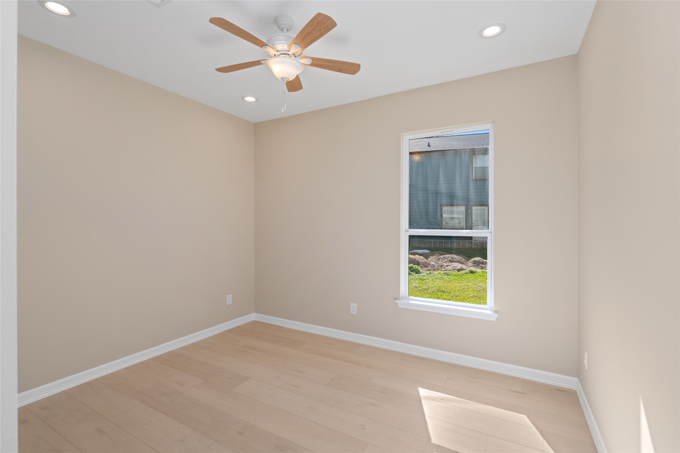 Bright secondary bedroom with large window and ceiling fan. Comfort, light, and style combine effortlessly.