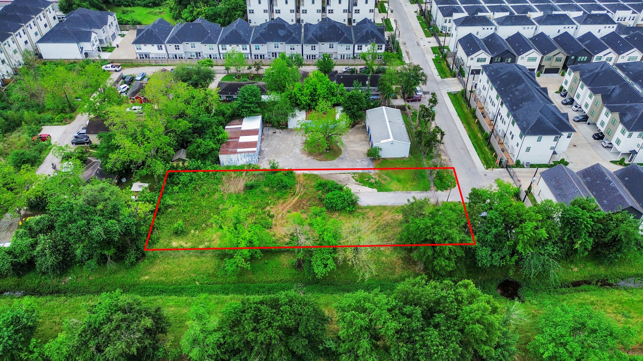 This aerial photo shows a rectangular plot of land outlined in red, surrounded by greenery. It's located in a residential neighborhood with nearby modern townhouses. The plot appears to be largely undeveloped, offering potential for building. This aerial photo shows a rectangular plot of land outlined in red, surrounded by greenery. It's located in a residential neighborhood with nearby modern townhouses. The plot appears to be largely undeveloped, offering potential for building.