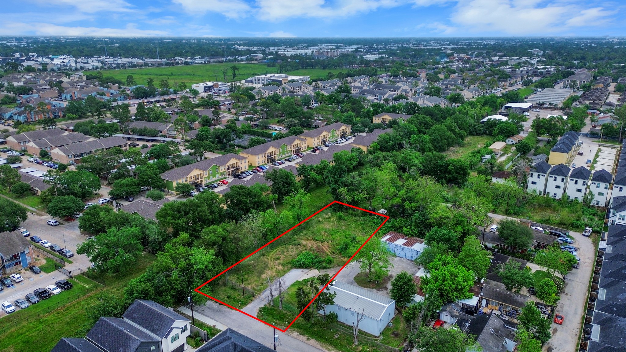 This photo shows a plot of land outlined in red, surrounded by greenery and trees in a residential neighborhood. Nearby are various houses and apartment buildings, providing a suburban setting. The area appears peaceful with ample space and potential for development. This photo shows a plot of land outlined in red, surrounded by greenery and trees in a residential neighborhood. Nearby are various houses and apartment buildings, providing a suburban setting. The area appears peaceful with ample space and potential for development.