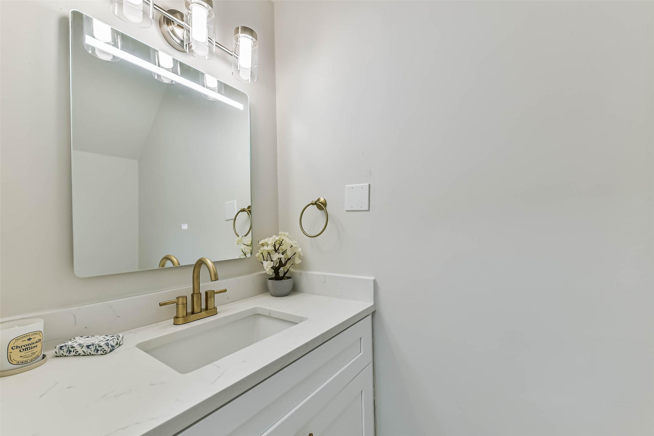 The half bathroom is located on the first floor with quartz counters, updated light fixture, gold fixtures and updated shaker style cabinetry.