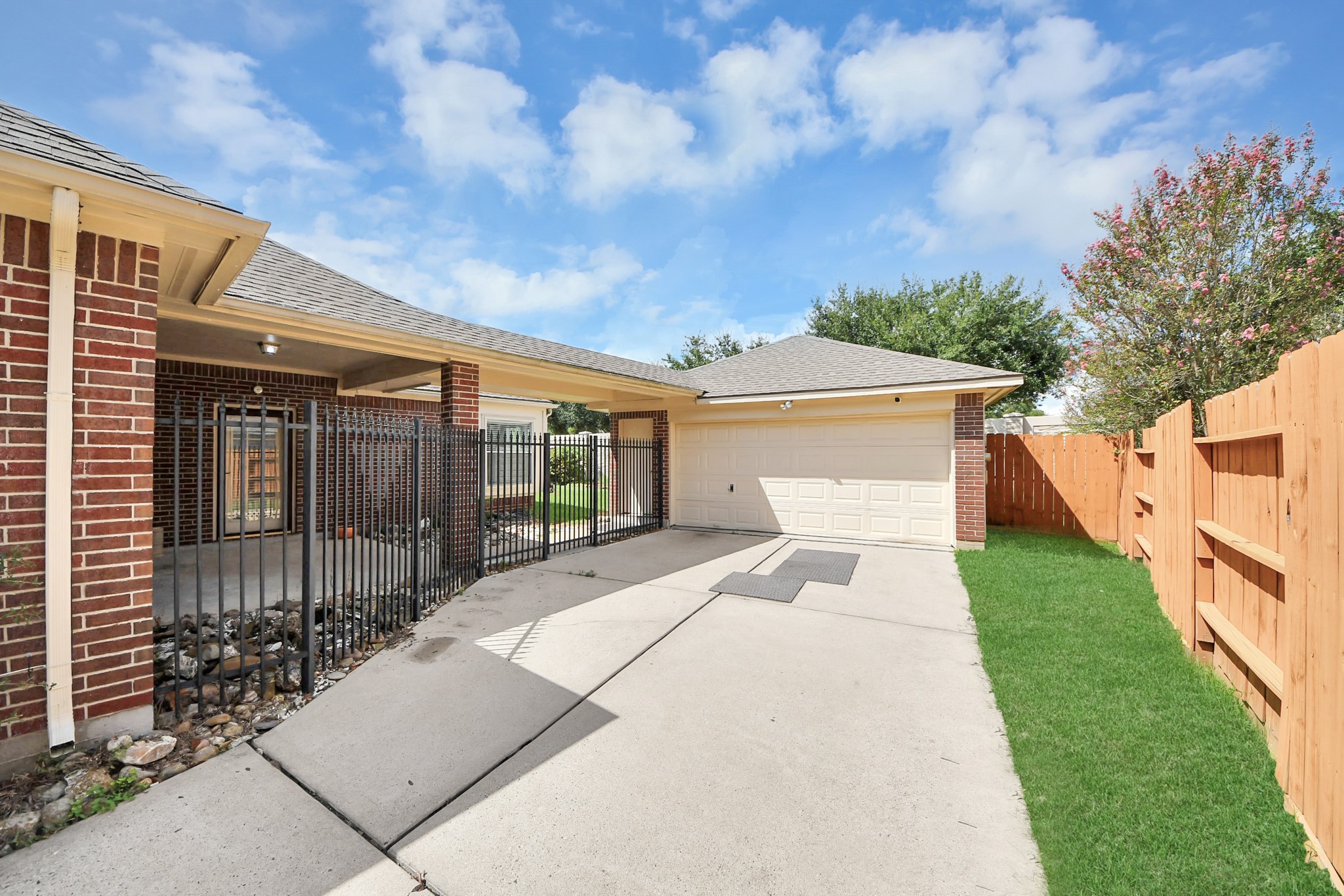 Spacious driveway leading to a two-car garage, complemented by a fenced side area and lush greenery, perfect for privacy and convenience.