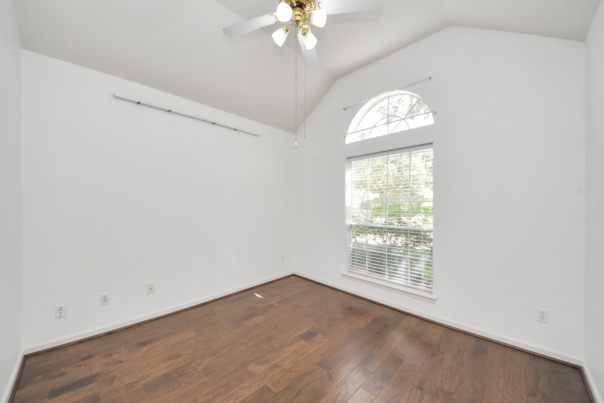 Bright room with vaulted ceiling, wood flooring, and a large window, perfect for natural light.