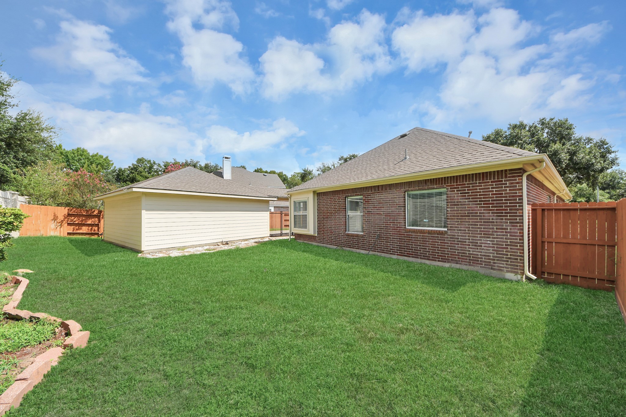 Spacious backyard with lush green lawn, bordered by a charming red brick exterior and a wooden fence for added privacy.