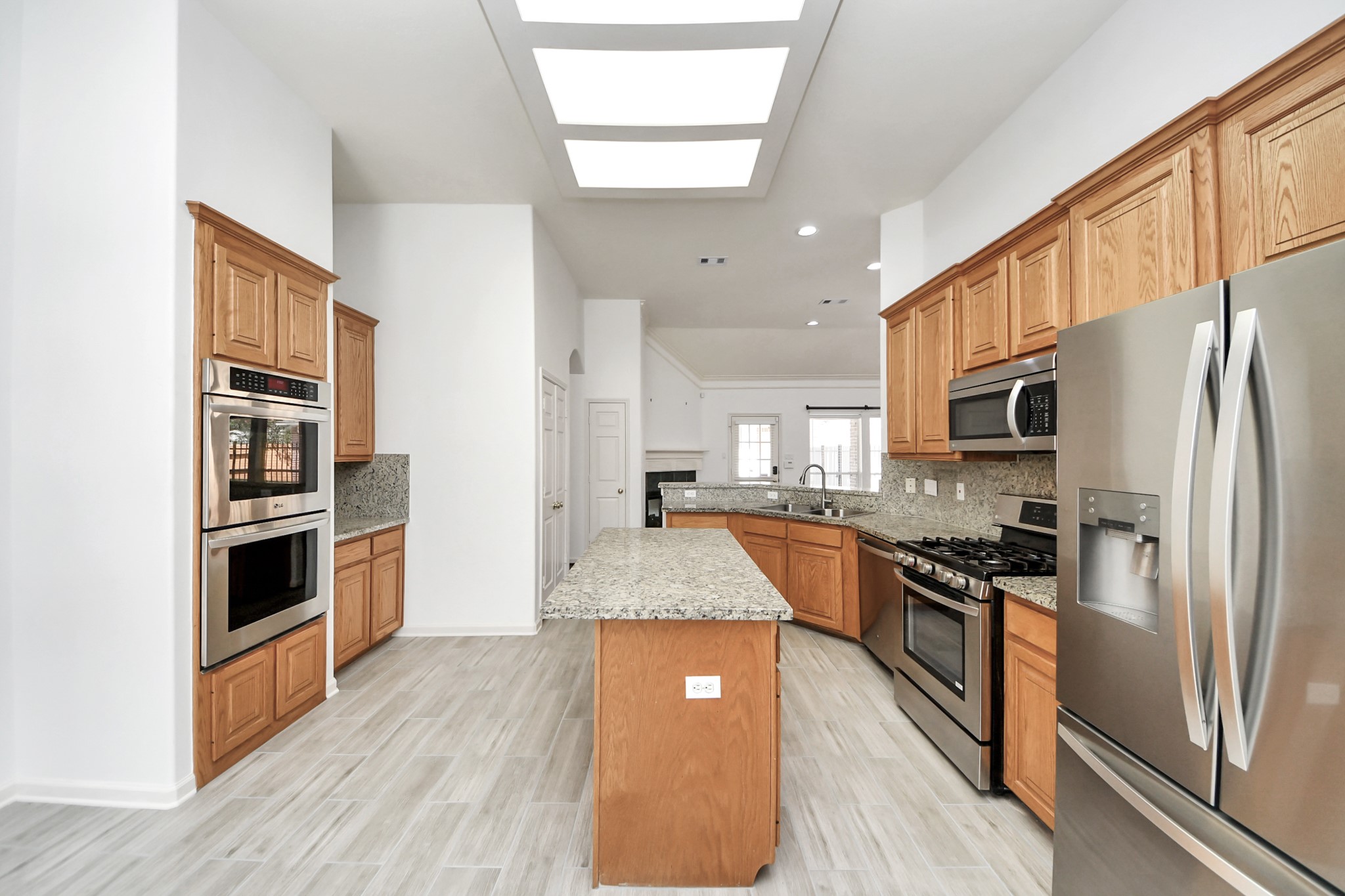 Spacious kitchen featuring granite countertops, stainless steel appliances, and ample wooden cabinetry, complemented by modern tile flooring and abundant natural light.