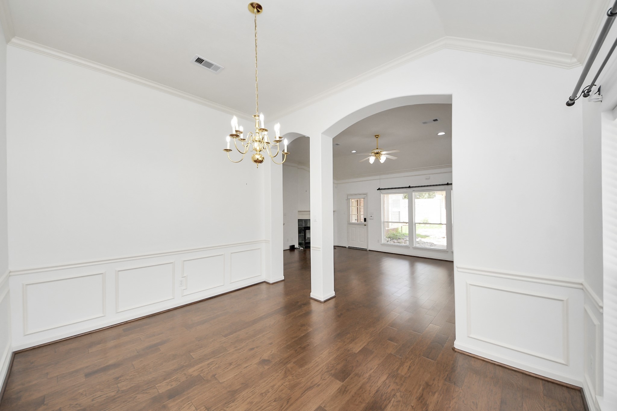 Elegant dining area with hardwood floors, wainscoting, and a classic chandelier, flowing seamlessly into a bright living space with large windows.