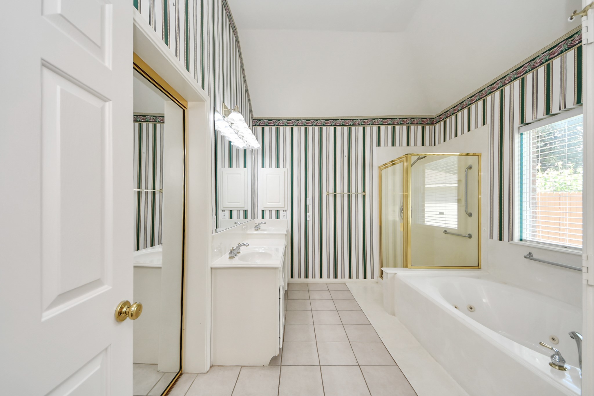 Spacious bathroom featuring a luxurious jetted tub, separate glass-enclosed shower, dual sinks, and elegant striped wallpaper.