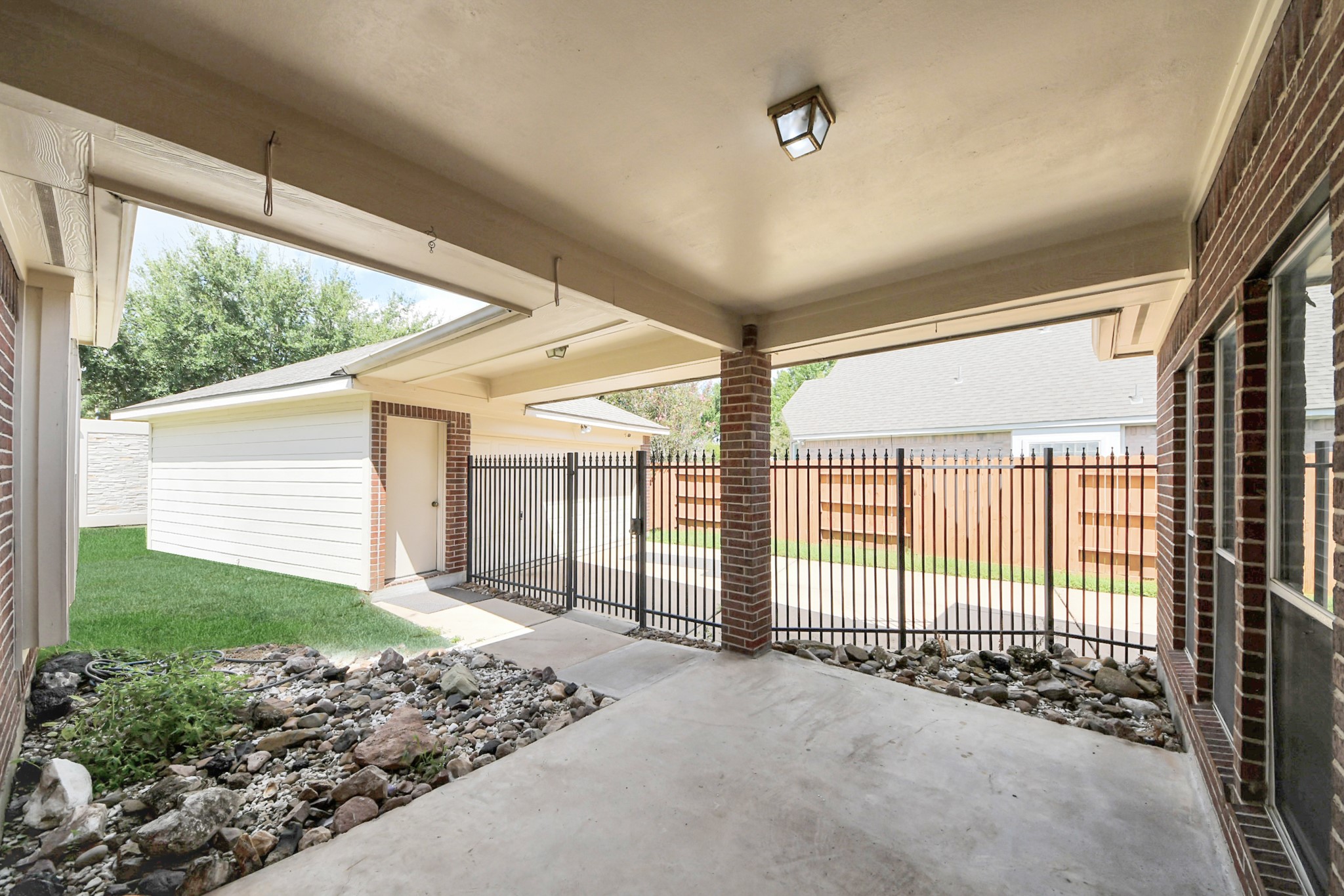 Spacious covered patio with brick accents, perfect for outdoor relaxation, overlooking a fenced yard with easy access to the garage.