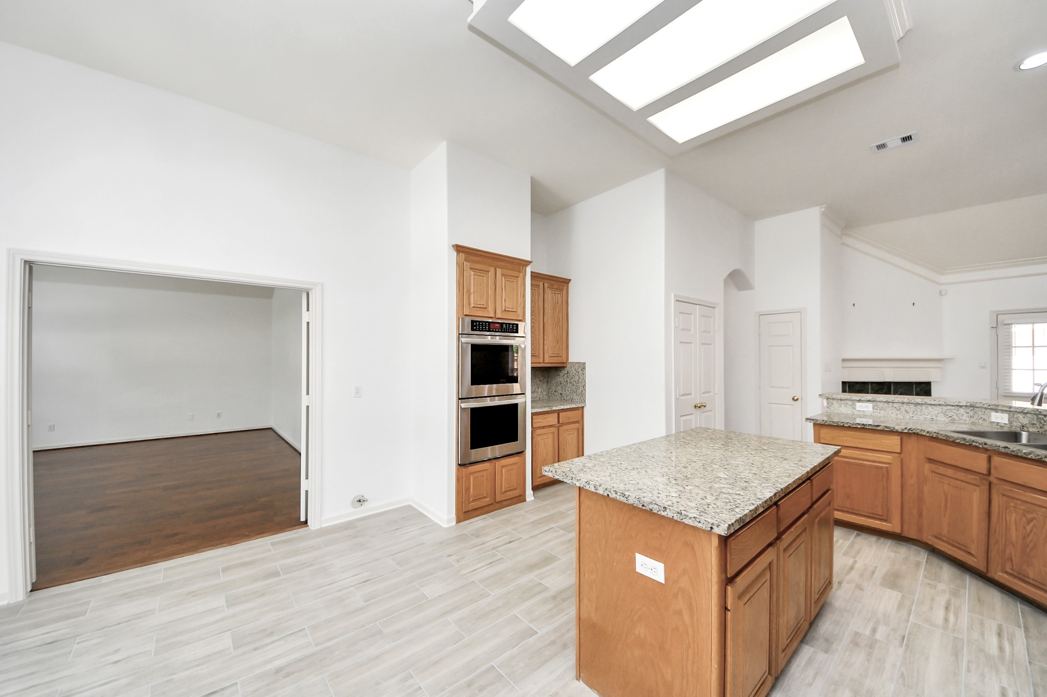 Spacious kitchen with granite countertops and wood cabinetry, featuring a central island and stainless steel appliances. Adjacent open living area with hardwood floors offers a seamless flow for entertaining.