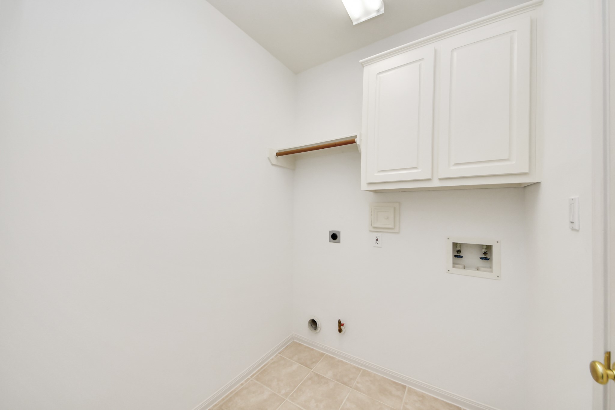 Spacious laundry room featuring tiled flooring, bright walls, and ample cabinetry for storage.