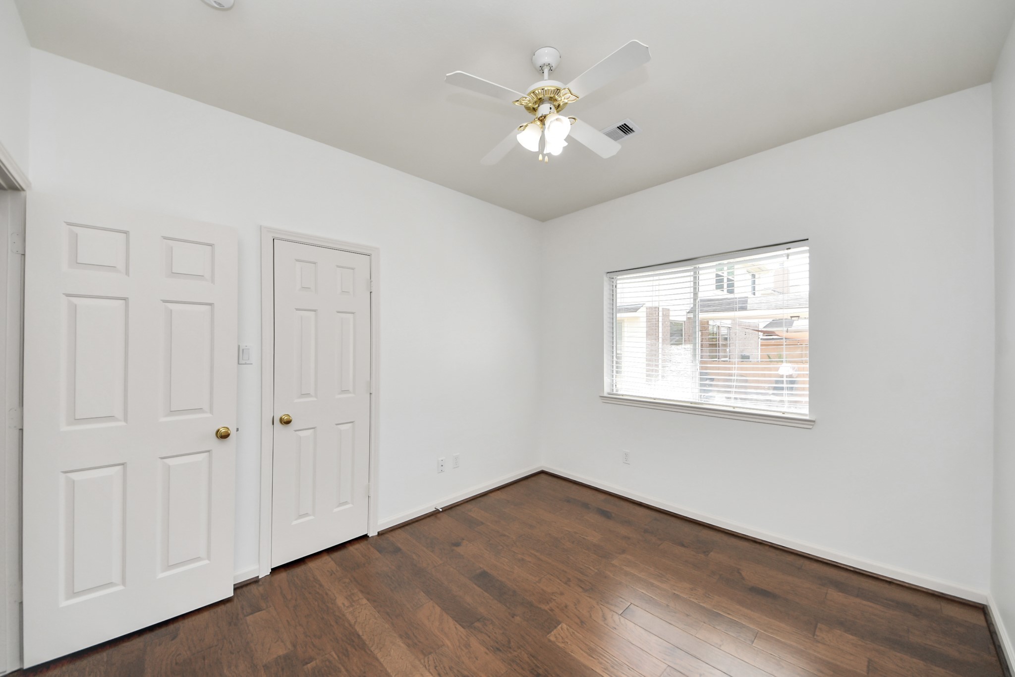 Bright and airy bedroom featuring hardwood flooring, a ceiling fan, and ample natural light from a large window.