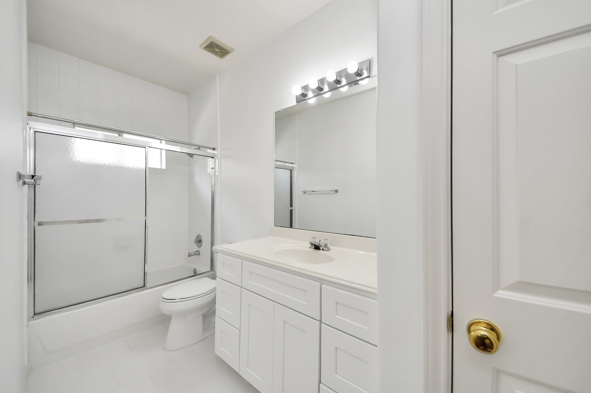Bright and clean bathroom featuring a sleek white vanity, spacious mirror with modern lighting, and a shower-tub combo with sliding glass doors.