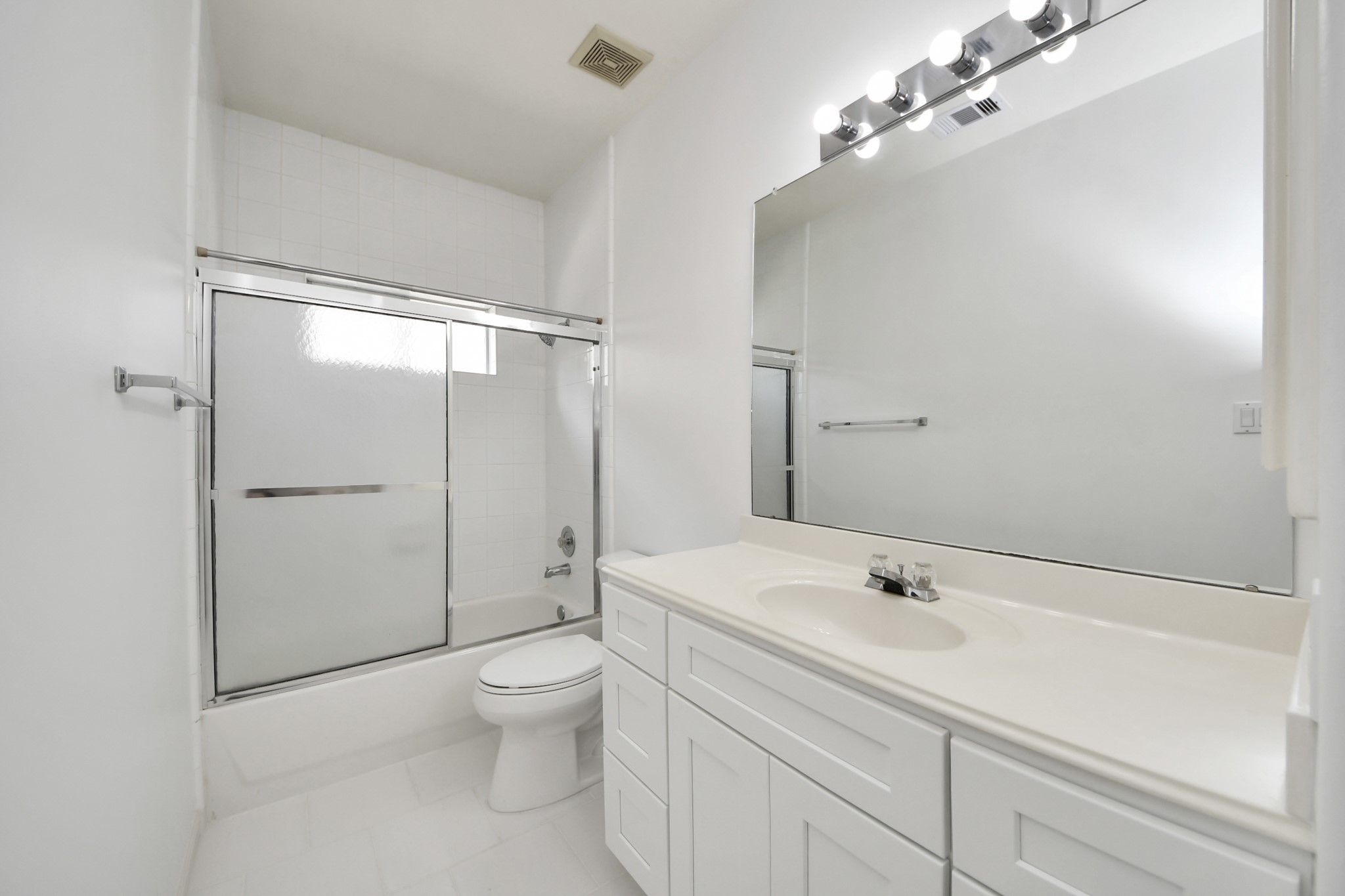 Bright and modern bathroom featuring a large mirror, sleek vanity with ample storage, and a glass-enclosed shower-tub combo.