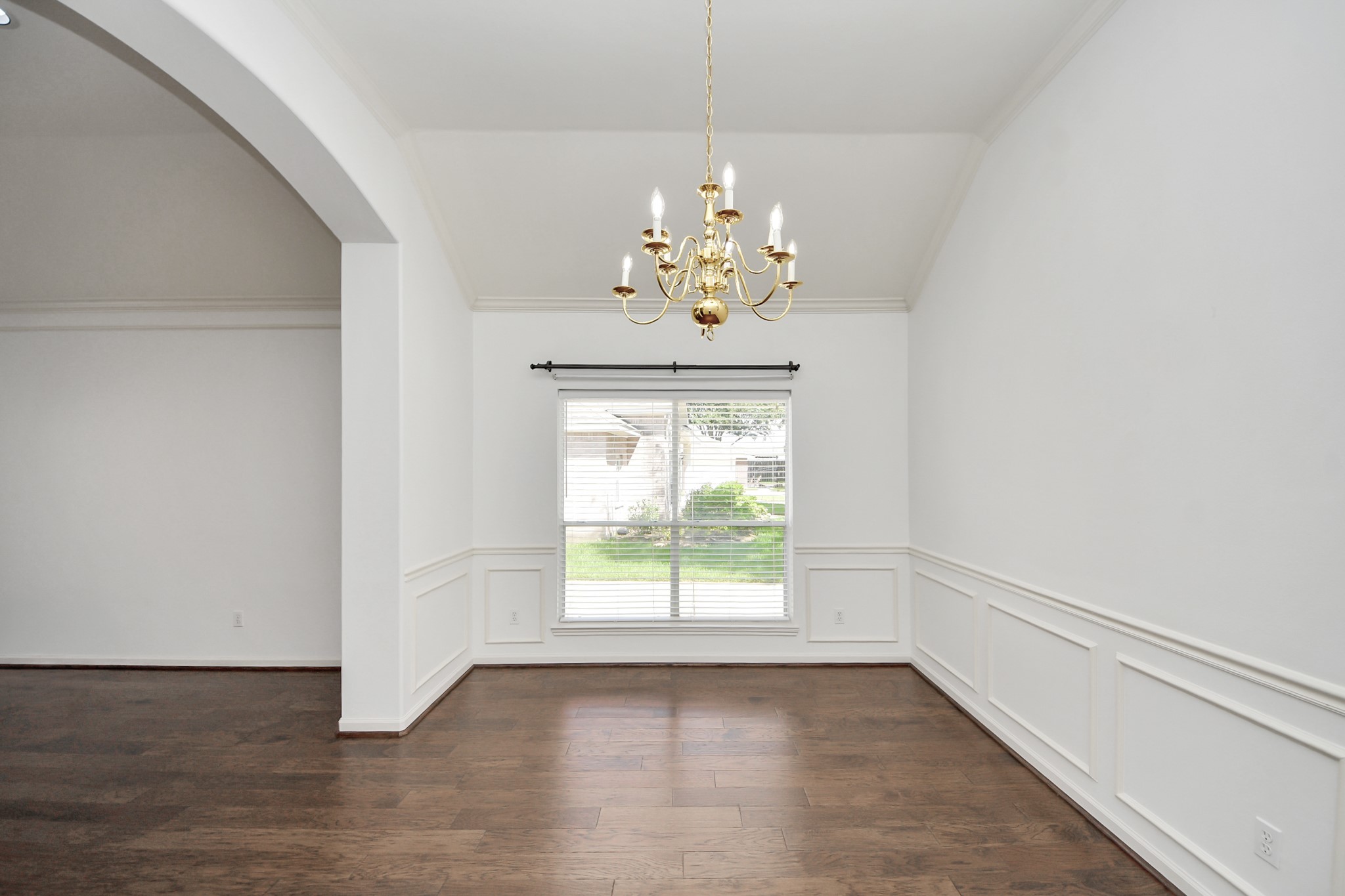 Elegant dining area with rich hardwood floors, a classic chandelier, and large window providing ample natural light.