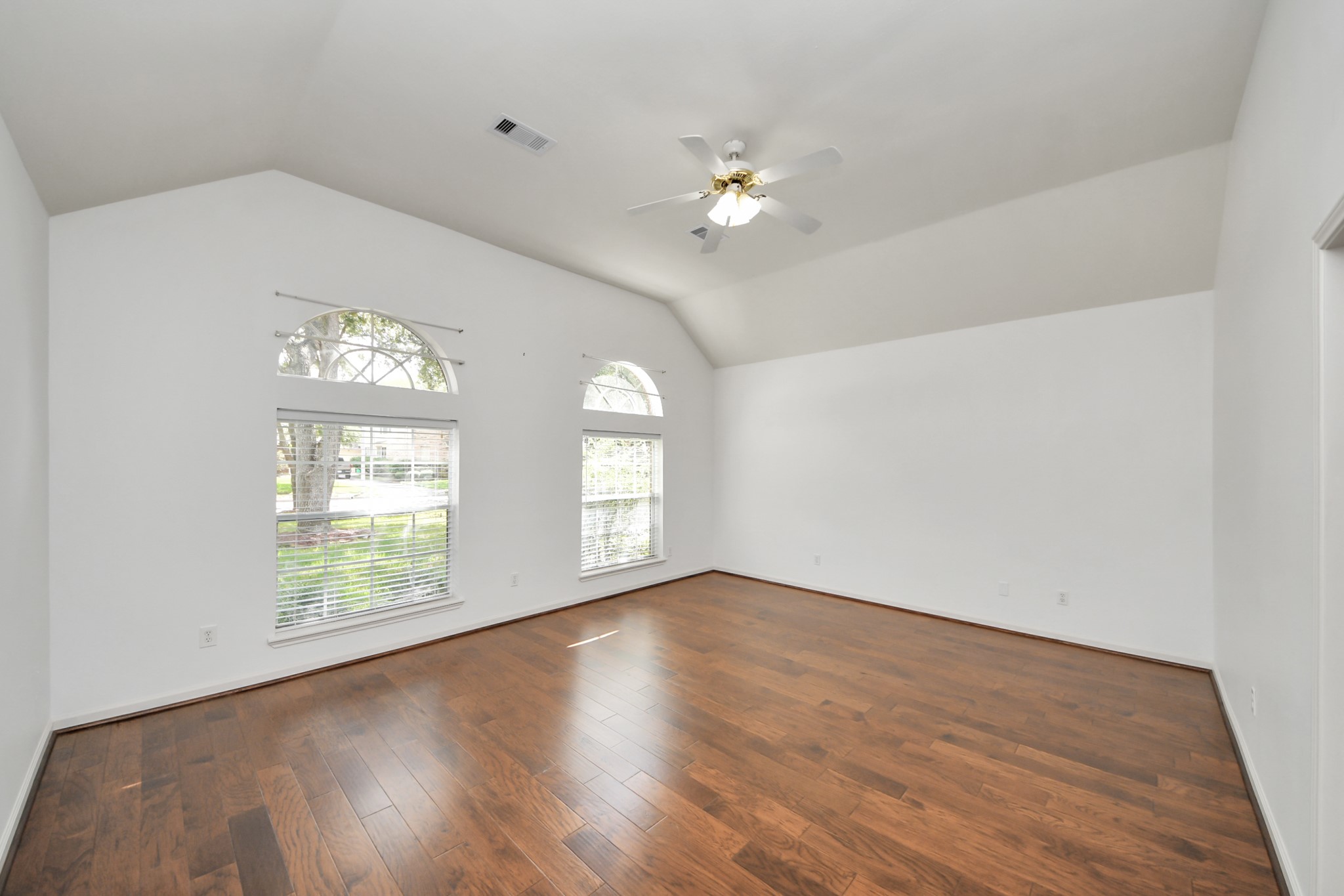 Spacious room with vaulted ceilings, rich hardwood floors, and abundant natural light from elegant arched windows.
